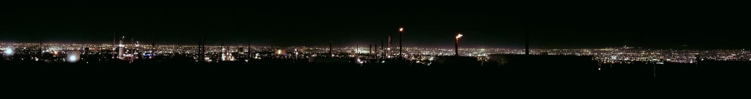 Night view of an industrial area with factories, smokestacks, and city lights in the distance.