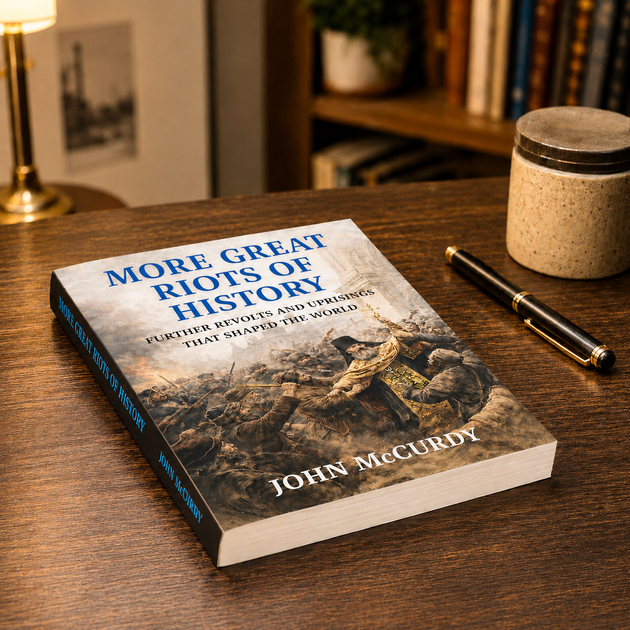 A book titled 'More Great Riots of History' on a wooden desk, with a pen and a ceramic container nearby, and a bookshelf in the background.