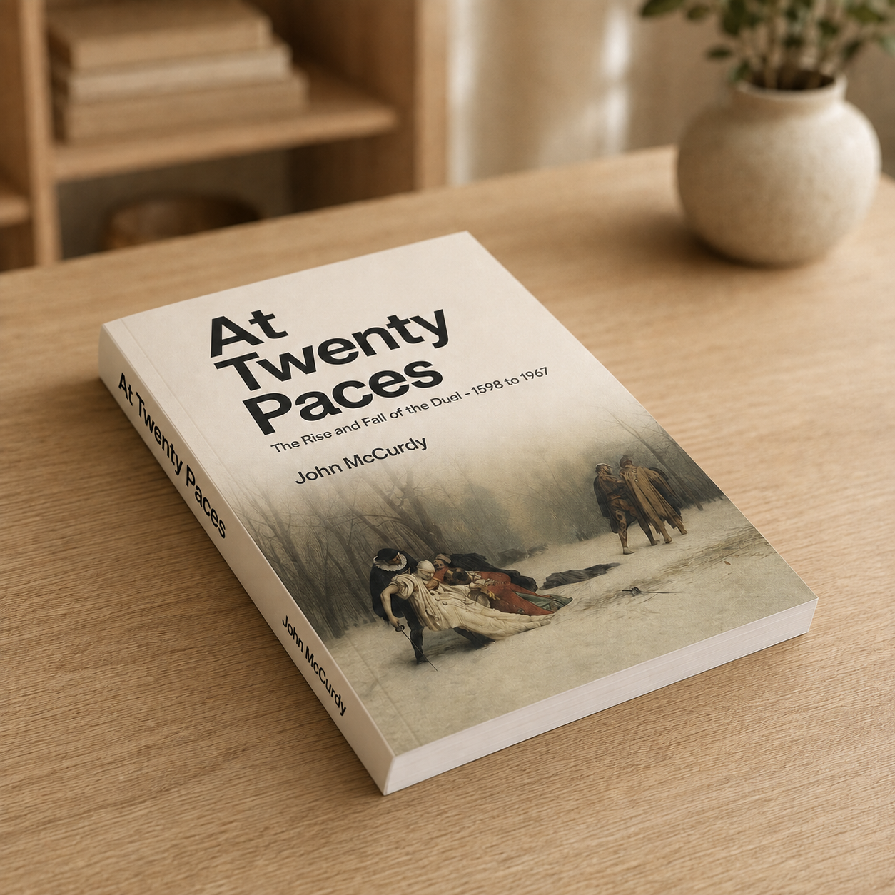 A book titled "At Twenty Paces" by John McCurdy lies on a light wooden table, with a small potted plant in the background.