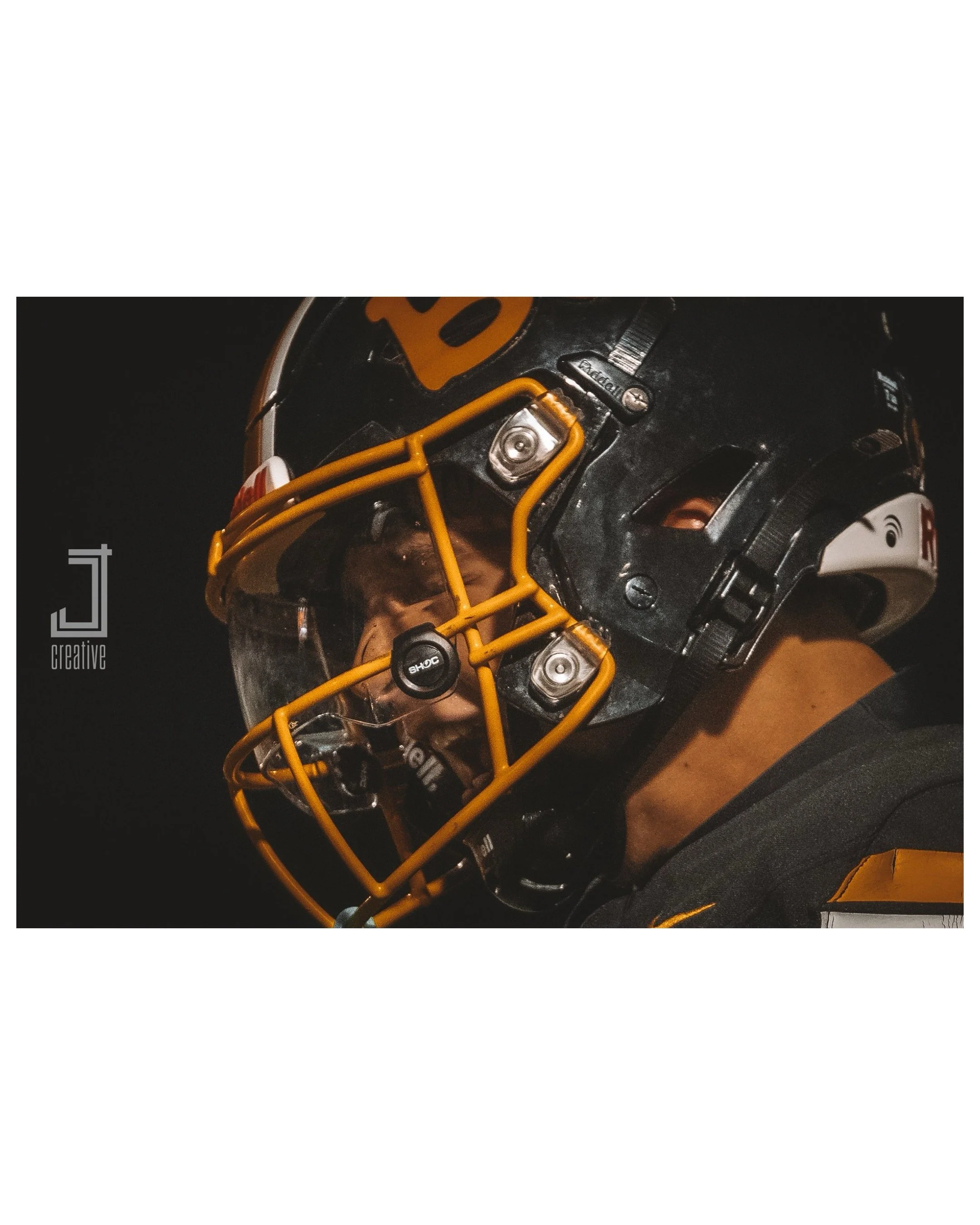Close-up of an American football helmet showing a black face mask with a yellow outline, and part of the helmet's black and orange design, on a dark background.