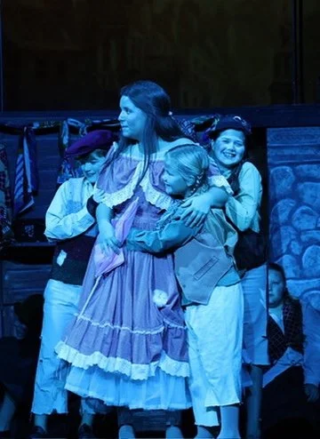 Children and a woman dressed in historical costumes, likely performing in a theater or play.