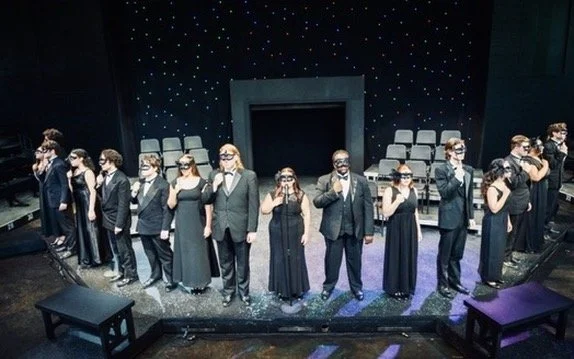 A group of people dressed in formal black attire standing in a line on a stage, wearing 3D glasses.