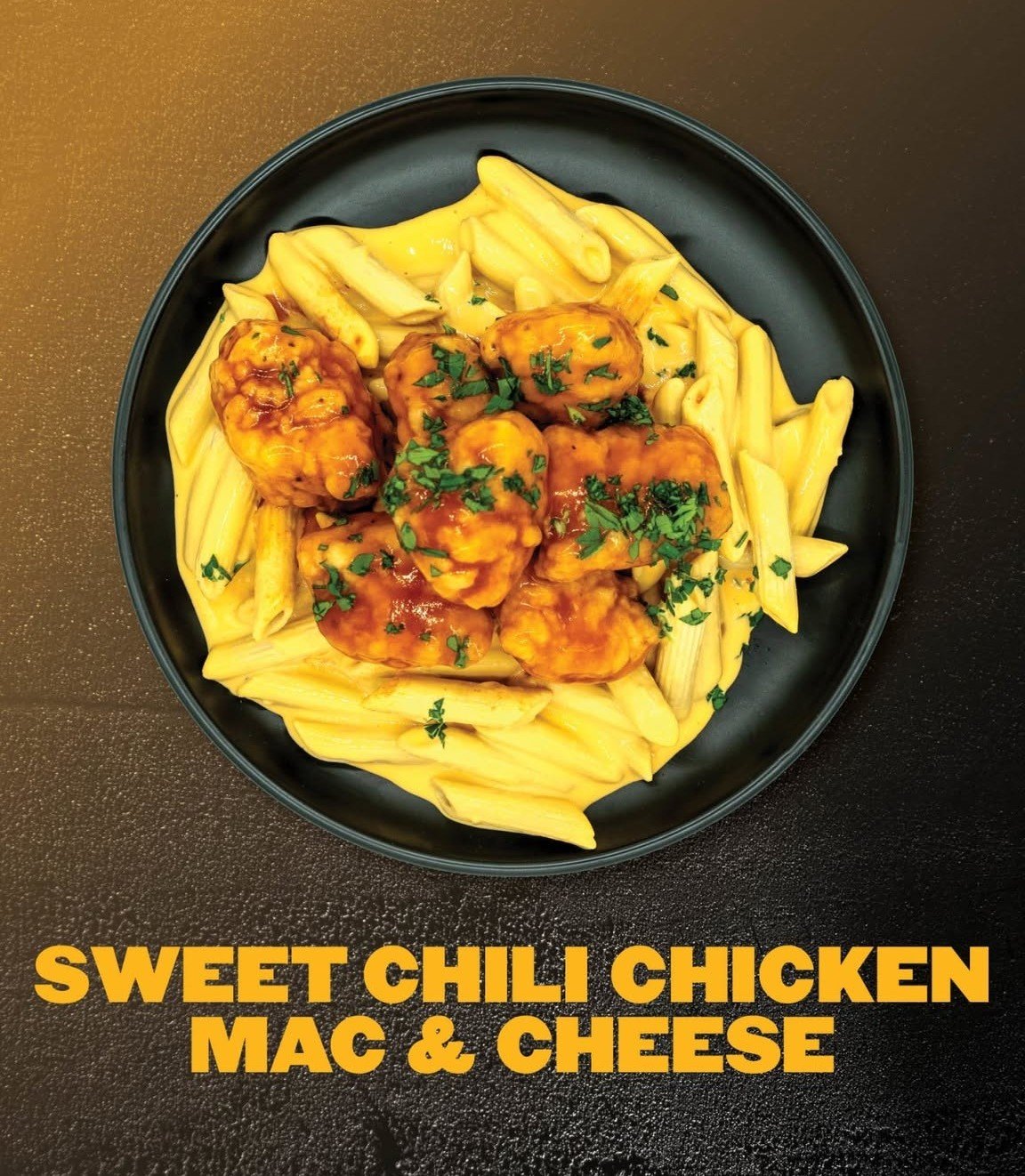A black bowl containing sweet chili chicken, macaroni and cheese, and penne pasta garnished with chopped parsley placed on a dark surface.