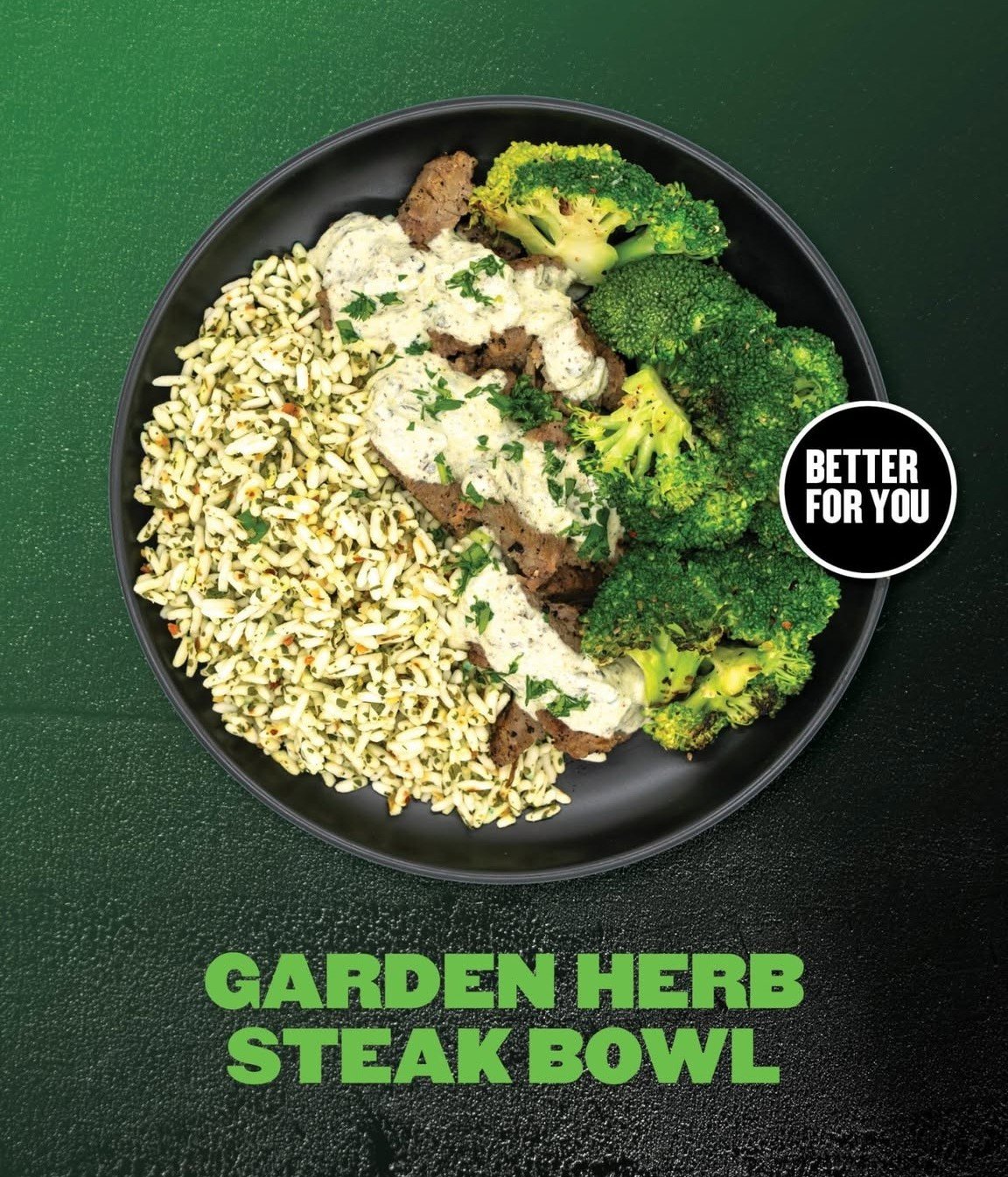 A black bowl containing cooked brown rice, broccoli florets, and sliced steak with herb sauce, on a green textured surface with the words 'Garden Herb Steak Bowl' in green text and a sticker saying 'Better for You'.