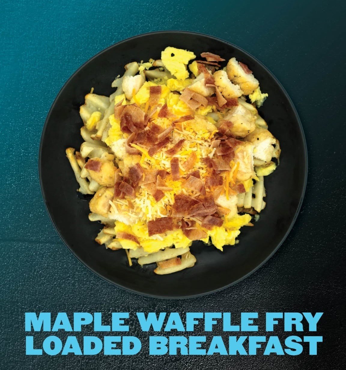 Black plate of maple waffle fry loaded breakfast with scrambled eggs, shredded cheese, and bacon pieces on a blue surface.
