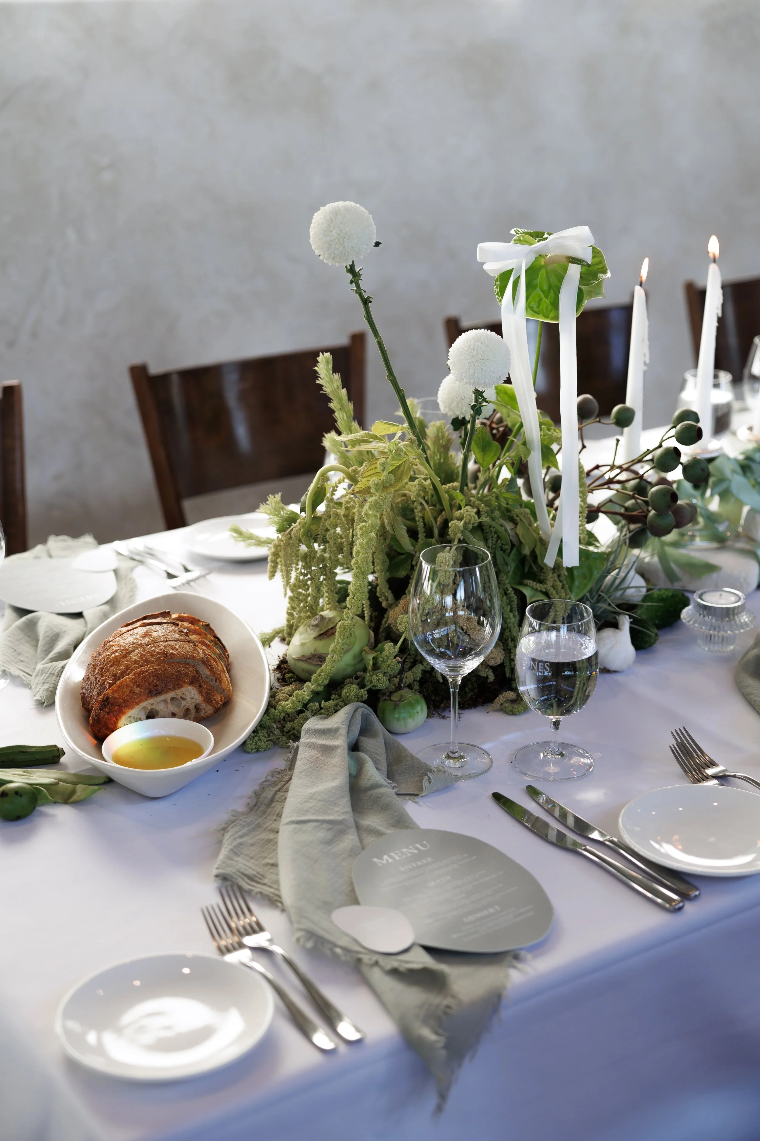 A decorated dining table with a floral centerpiece, candles, wine glasses, and tableware in a minimalist style, set for a formal meal.