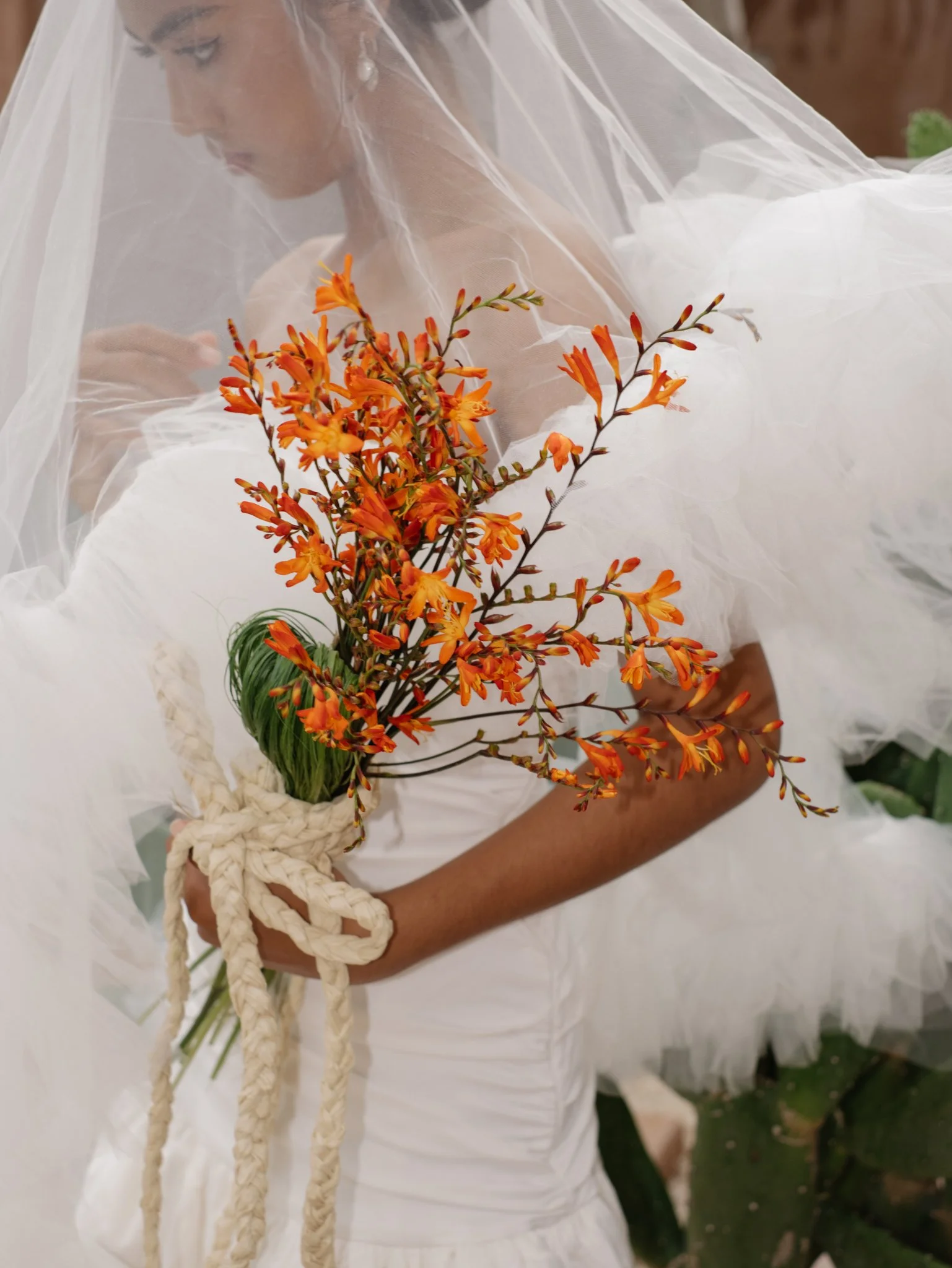 A person holding a bouquet of orange flowers with a white sheet or veil partially covering them.