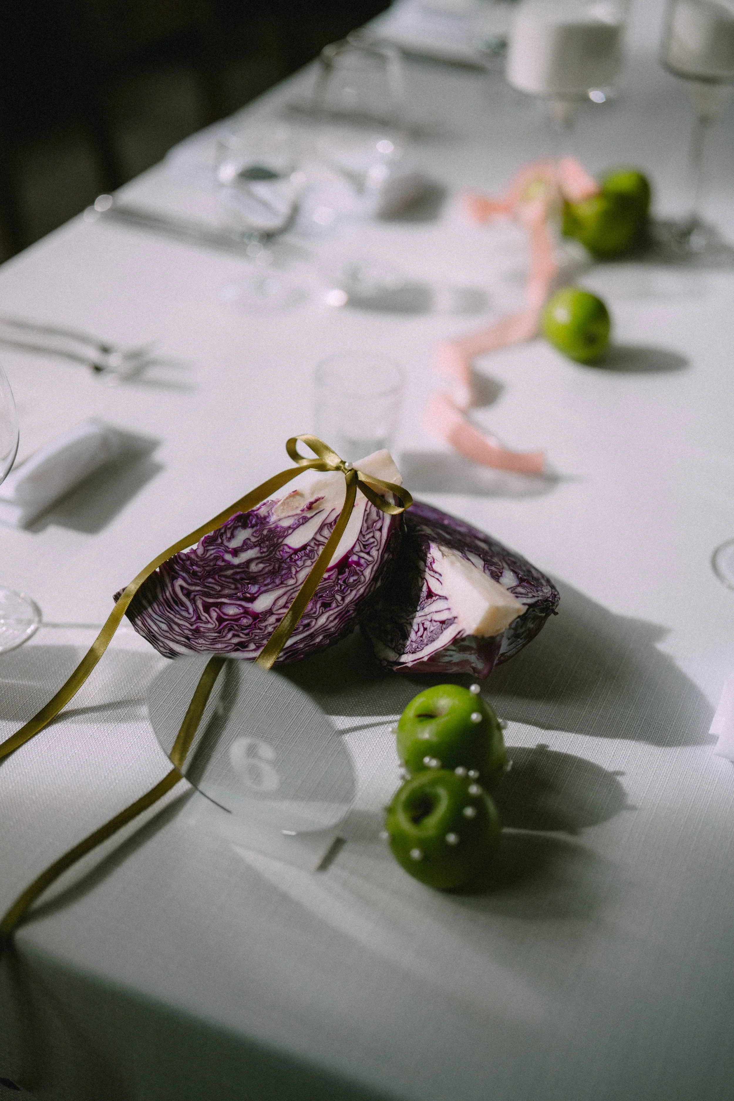 A table set with glassware, green apples, and a slice of purple and white marbled cake with a gold ribbon. The focus is on the cake and the apples in front of it.