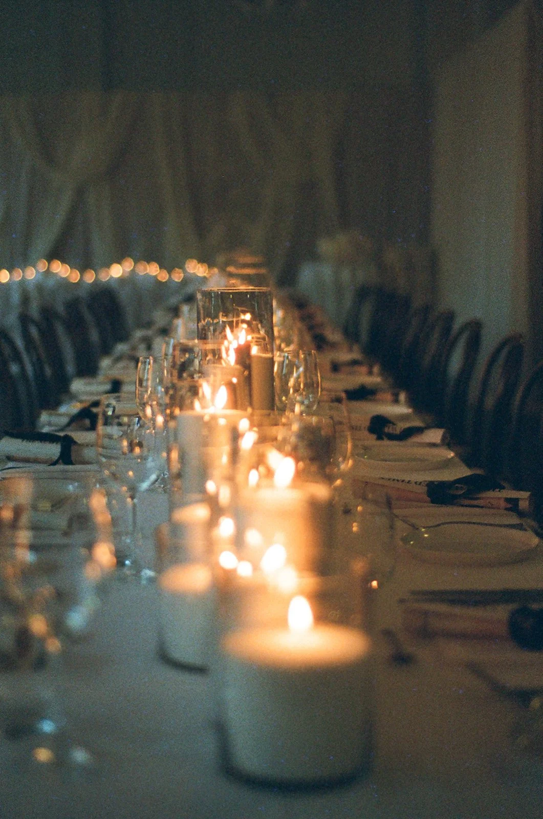 A long dining table set for an event with candles and wine glasses, created with warm, ambient lighting.