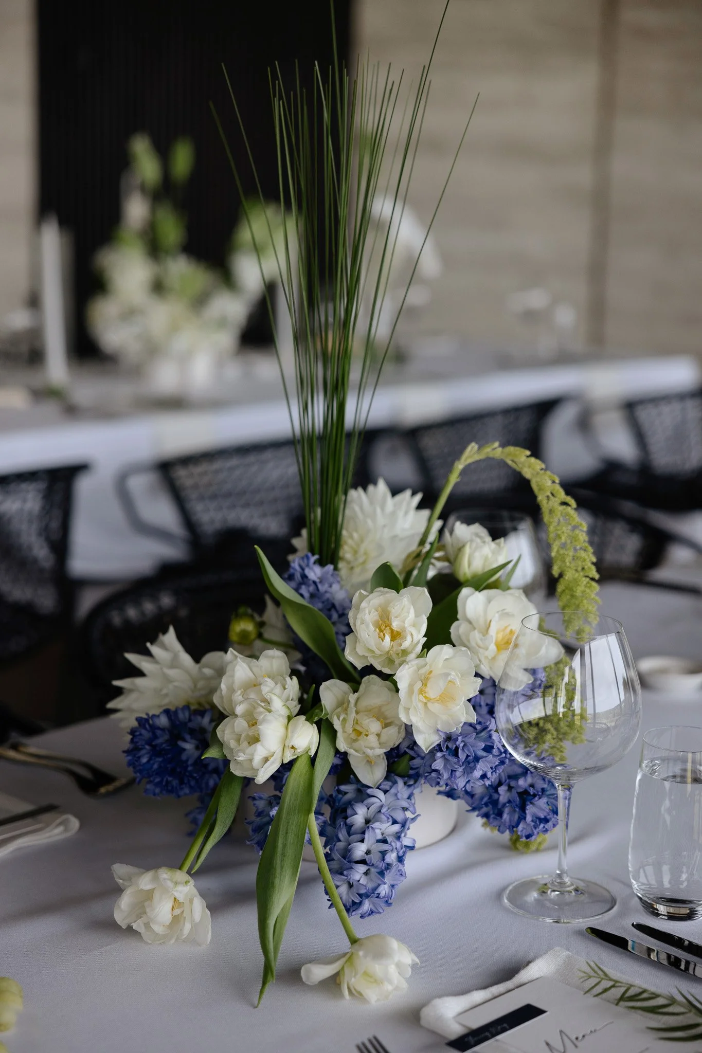 A floral centerpiece with white, purple, and yellow flowers on a dining table, with wine glasses and table settings visible.