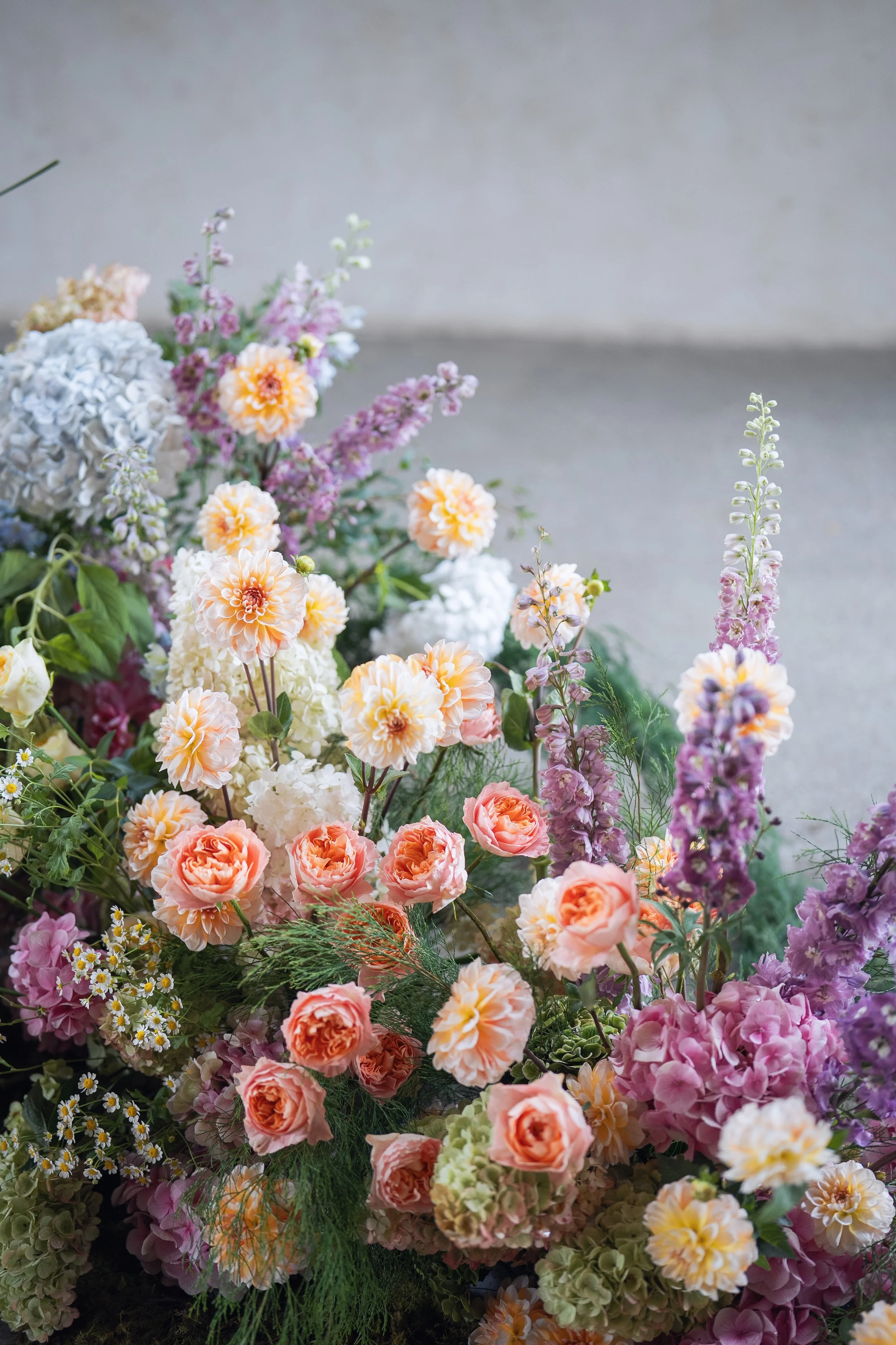 A vibrant arrangement of various colorful flowers including roses, hydrangeas, and snapdragons in soft pastel shades with green foliage.