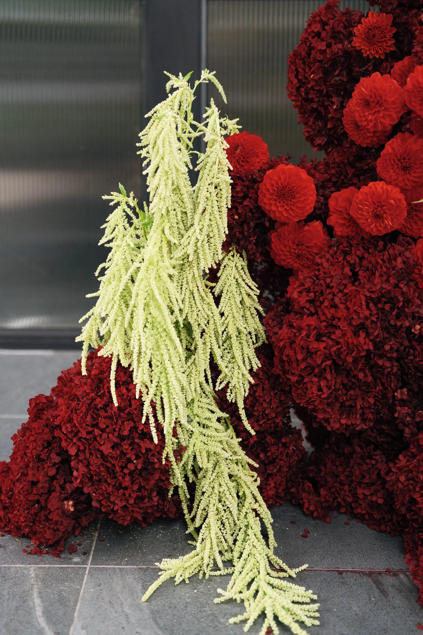 Wreath made of red flowers with long, hanging white flowers in front of it, placed on a tiled floor.
