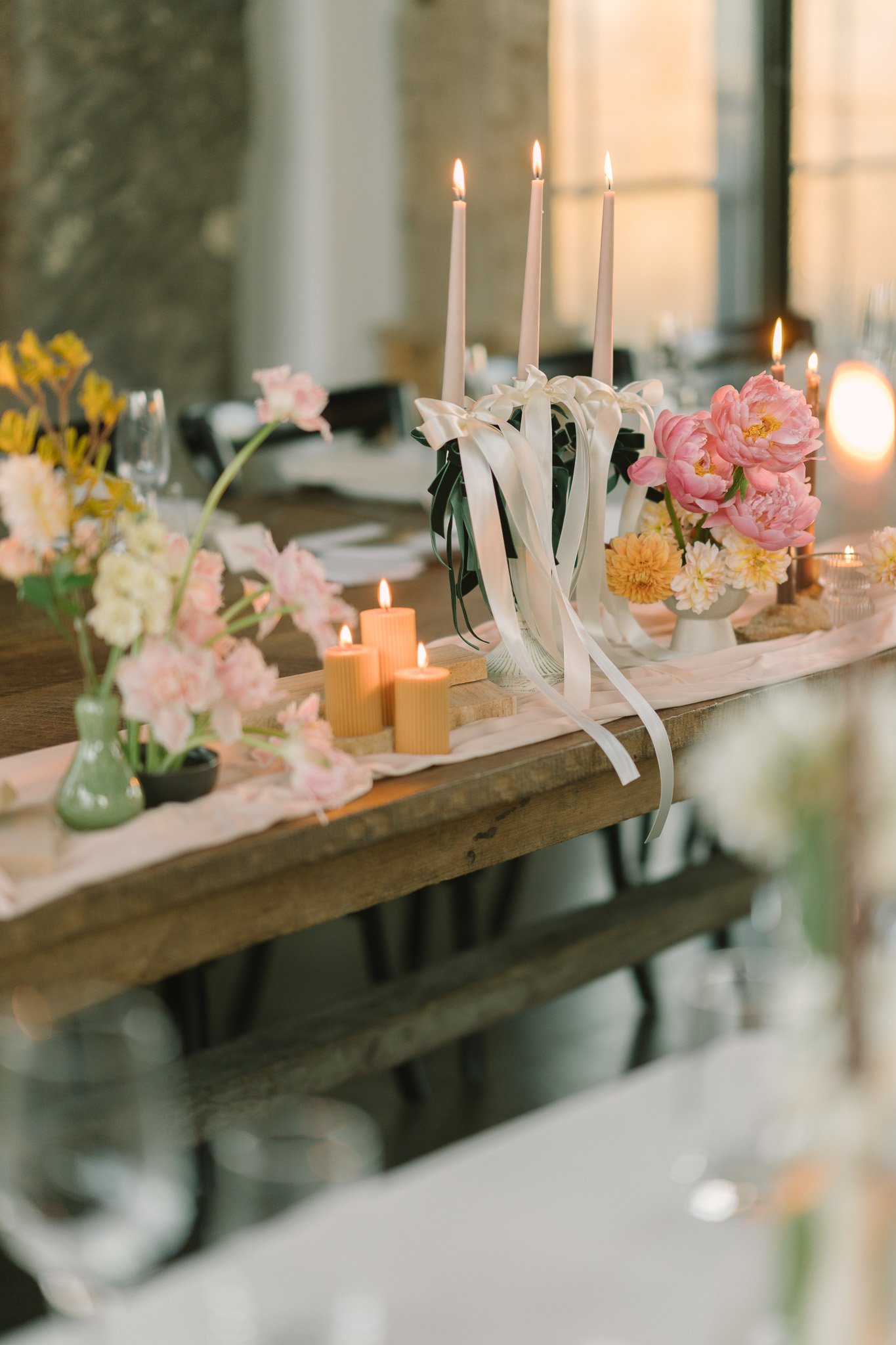 Decorative table setting with pink and white flowers, lit candles, and white taper candles tied with ribbons