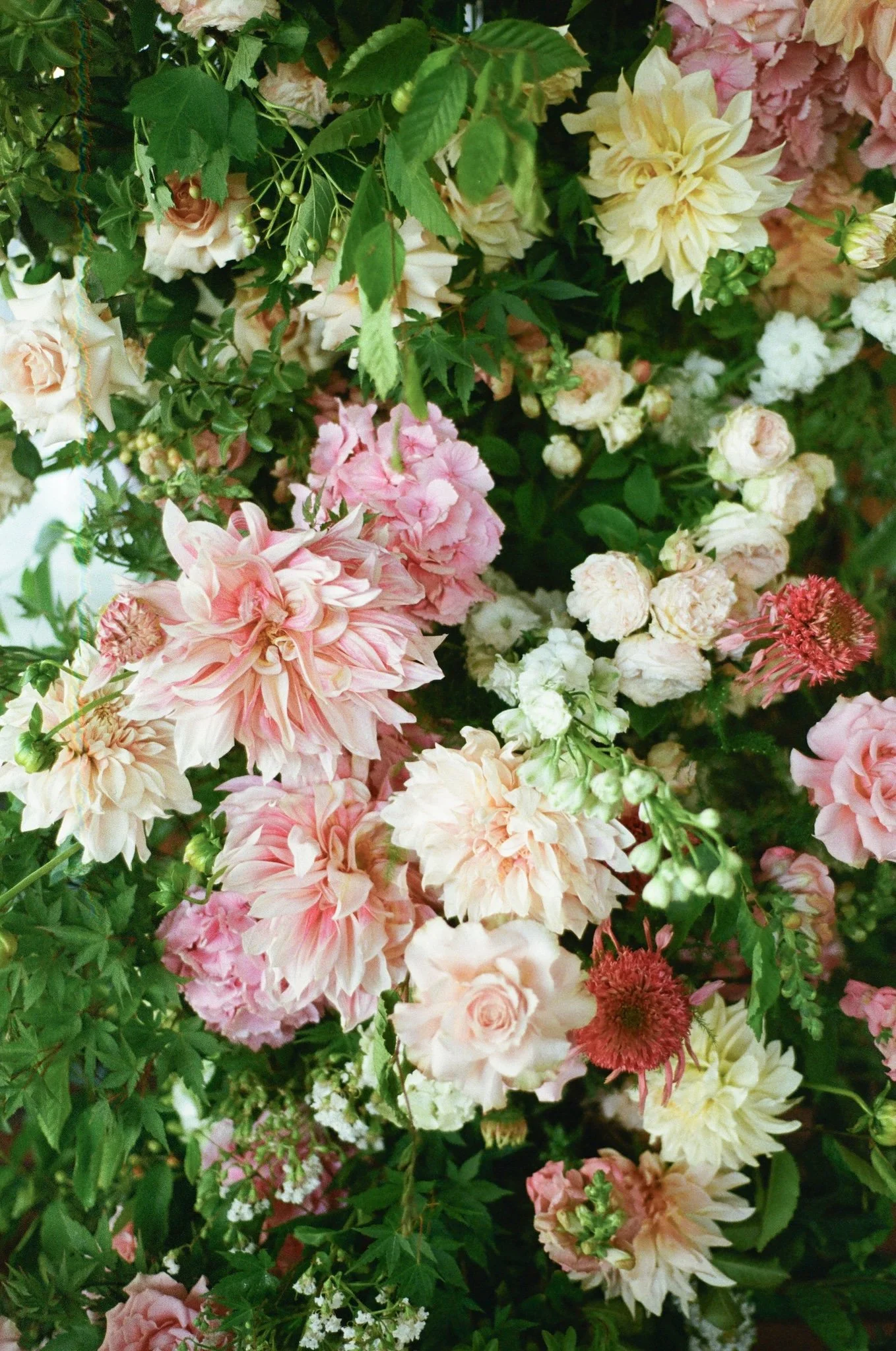 A dense arrangement of various flowers including pink roses, white carnations, yellow dahlias, and other colorful blooms with green foliage.