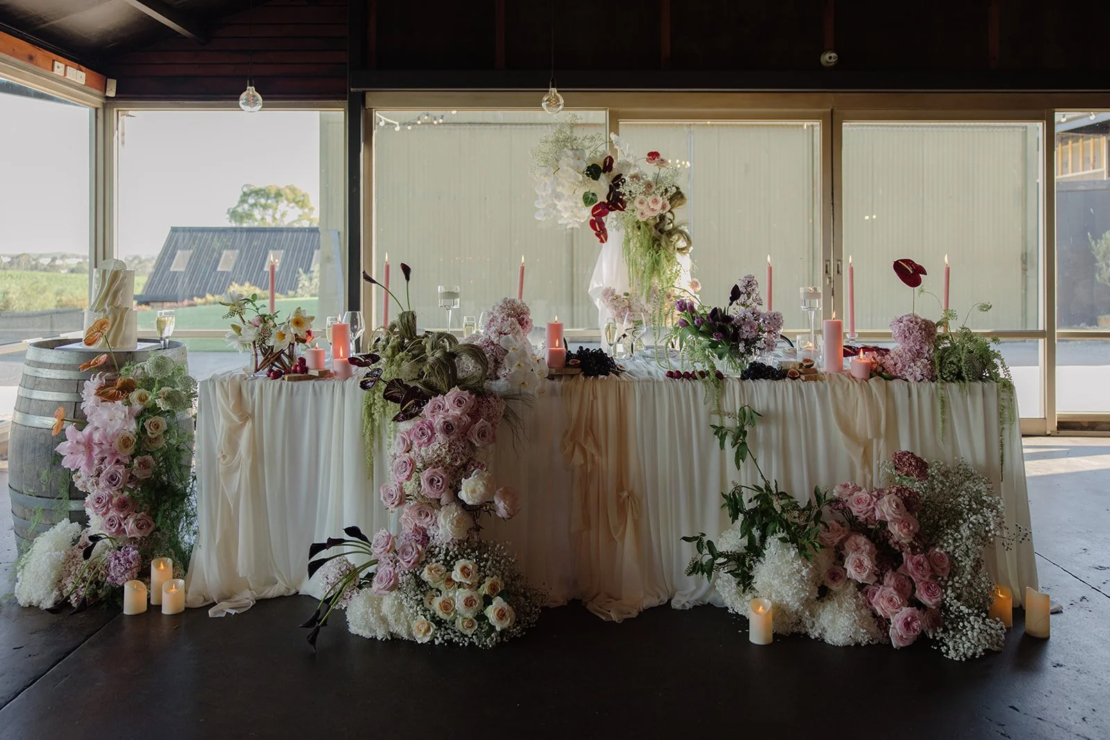 A decorated table with flowers, candles, and candles atop, set up indoors with large windows revealing a scenic outdoor view.