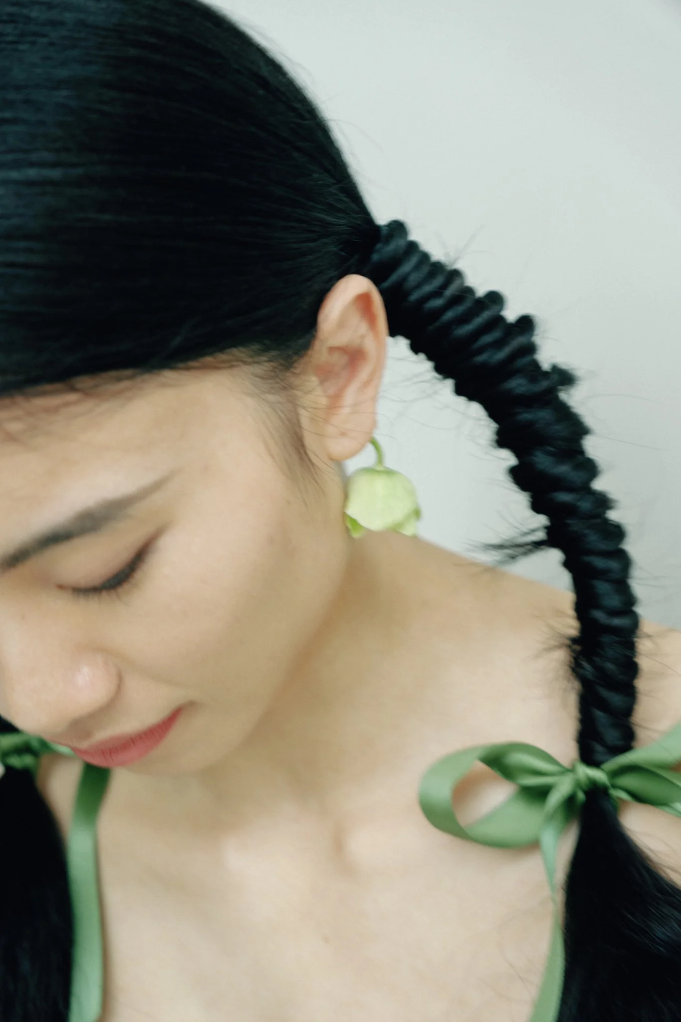A close-up of a woman with black hair styled in a spiral braid, wearing a green leaf-patterned outfit and a green flower earring.