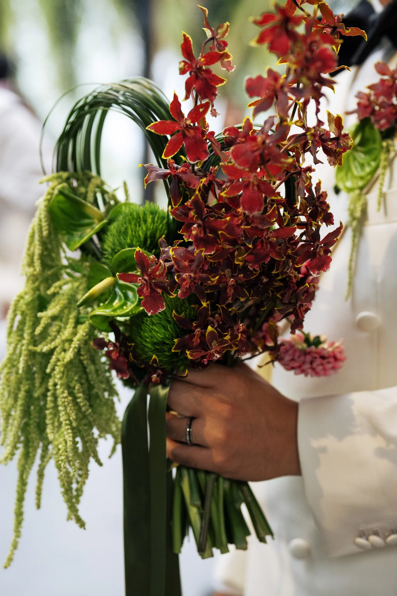 Close-up of a person holding a colorful bouquet of flowers, including red and green blossoms, with blurred background.