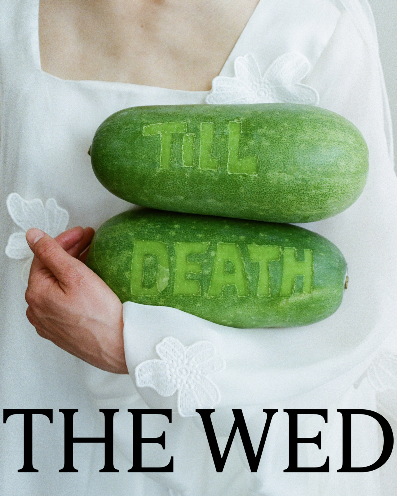 A person holding two green squash with the words "TILL" and "DEATH" carved into them. The person is wearing a white shirt with floral embroidery.