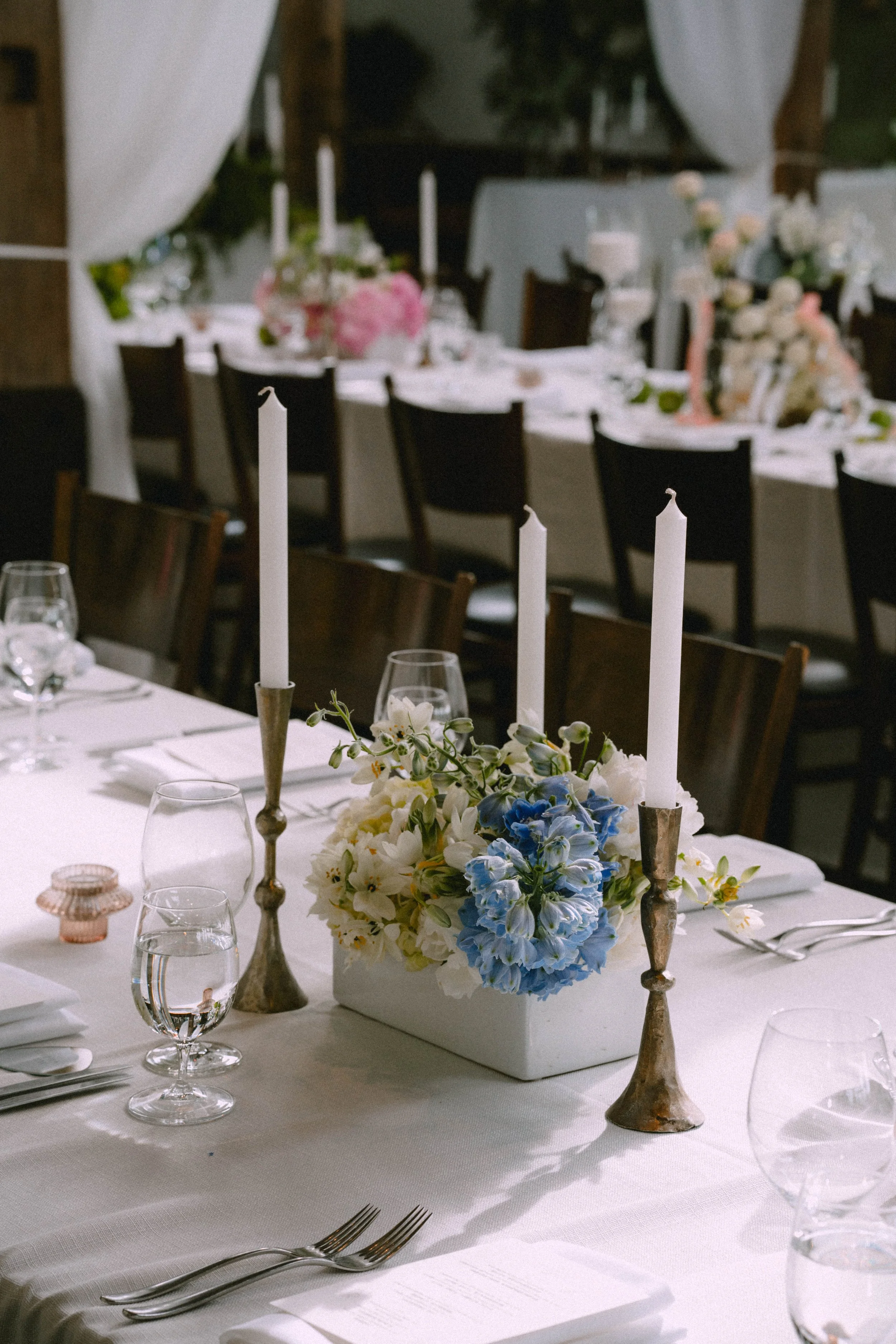 A decorated banquet table set for a formal event with floral centerpieces, tall candles, glassware, and silverware, featuring a white tablecloth and elegant decor.