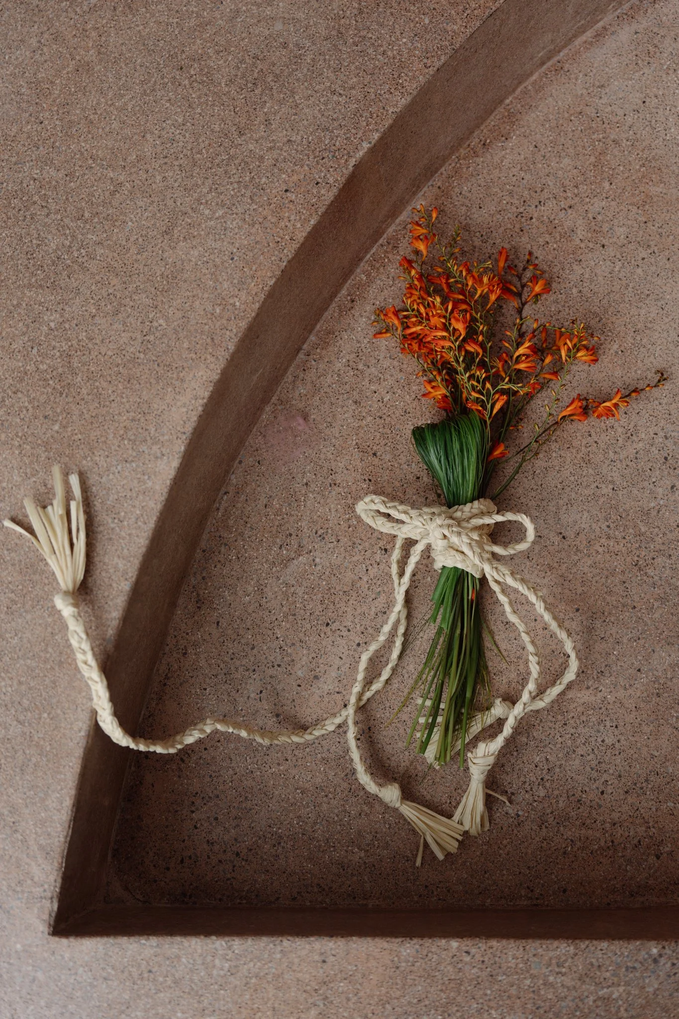 A bouquet of orange flowers with green leaves tied with a white rope, placed inside a rectangular planter.