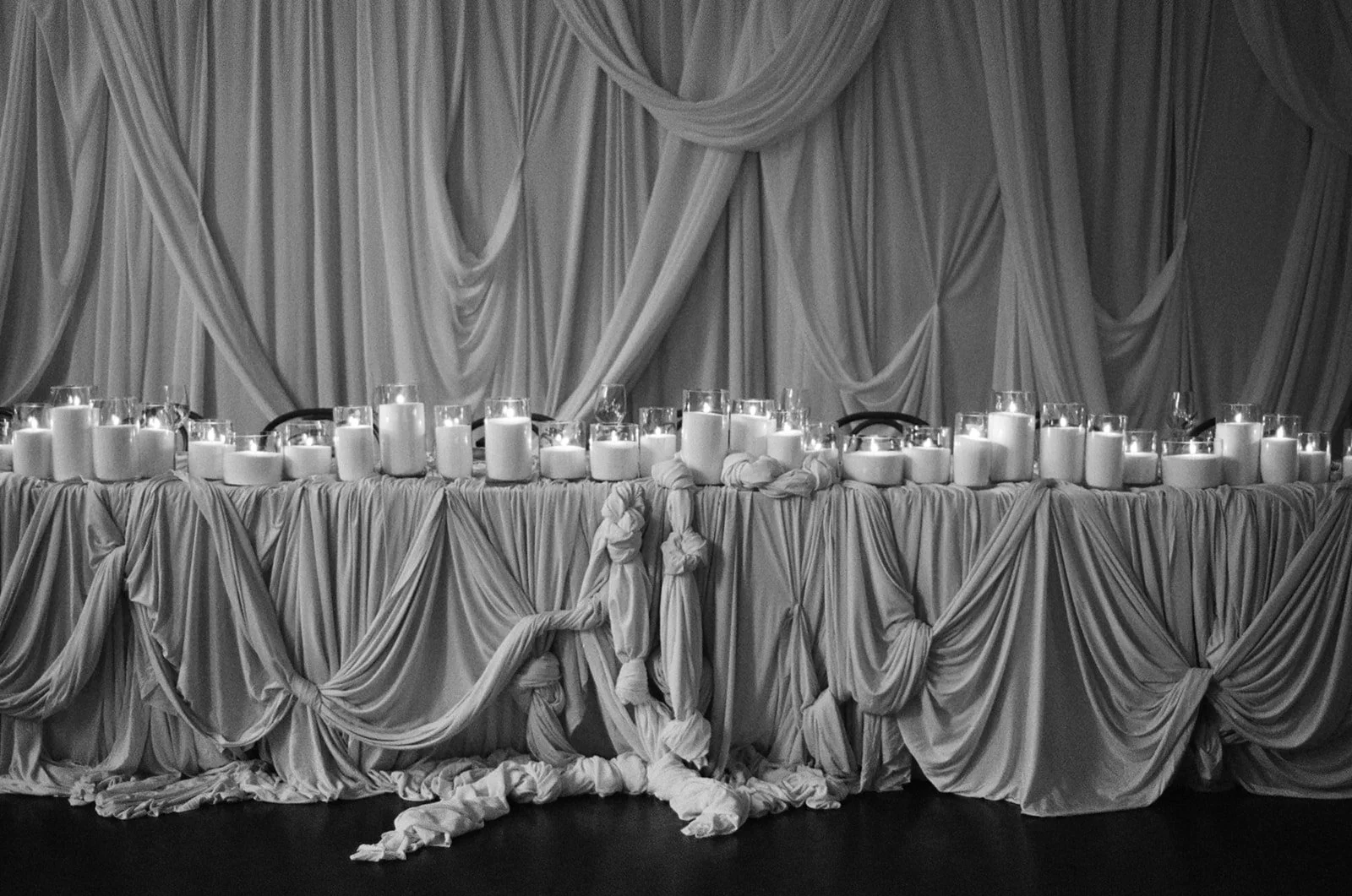 A draped table with candles and fabric decorations in a monochrome setting.