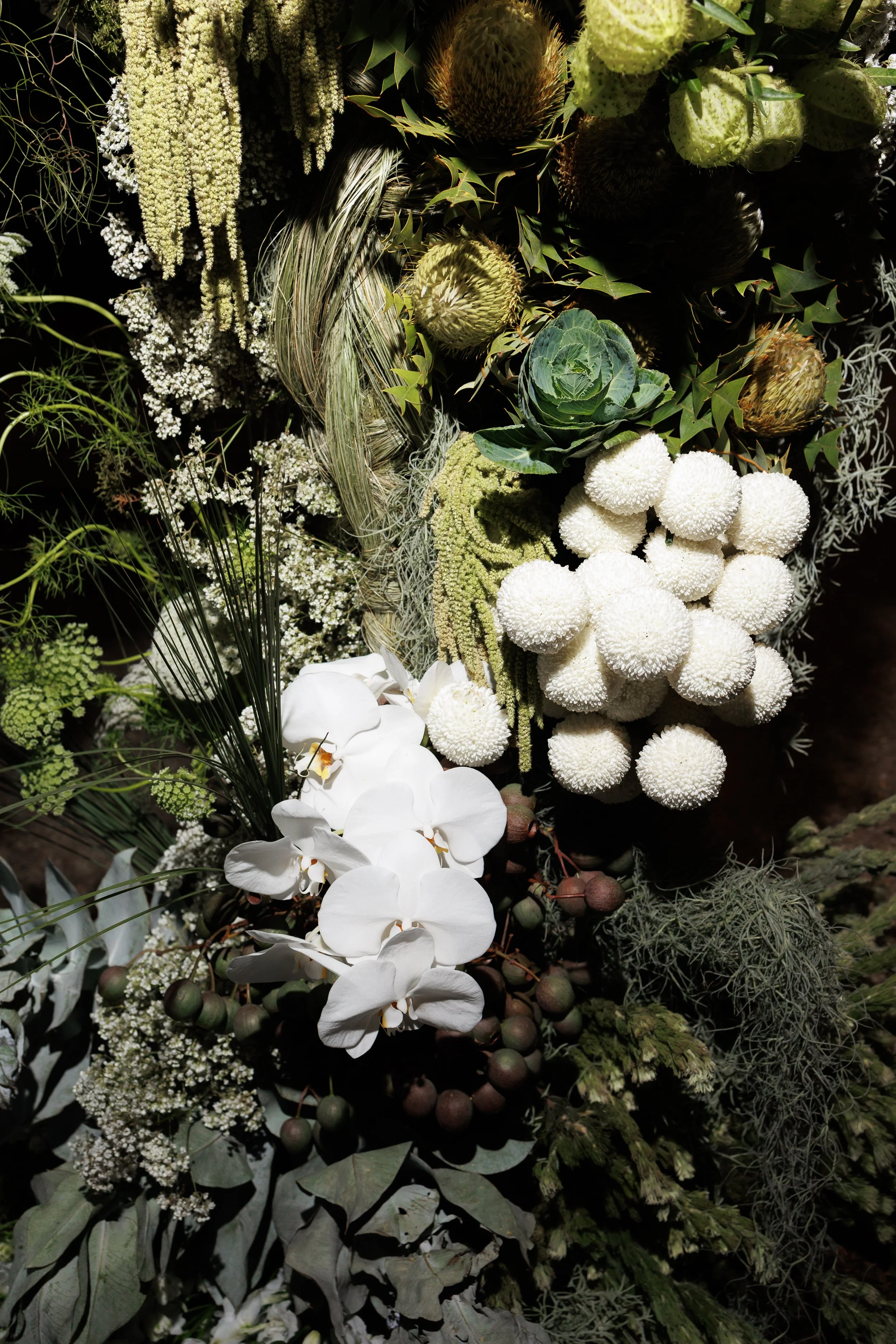 A dense arrangement of various white and green flowers and foliage, including orchids, chrysanthemums, succulents, and assorted greenery, creating a lush floral display.