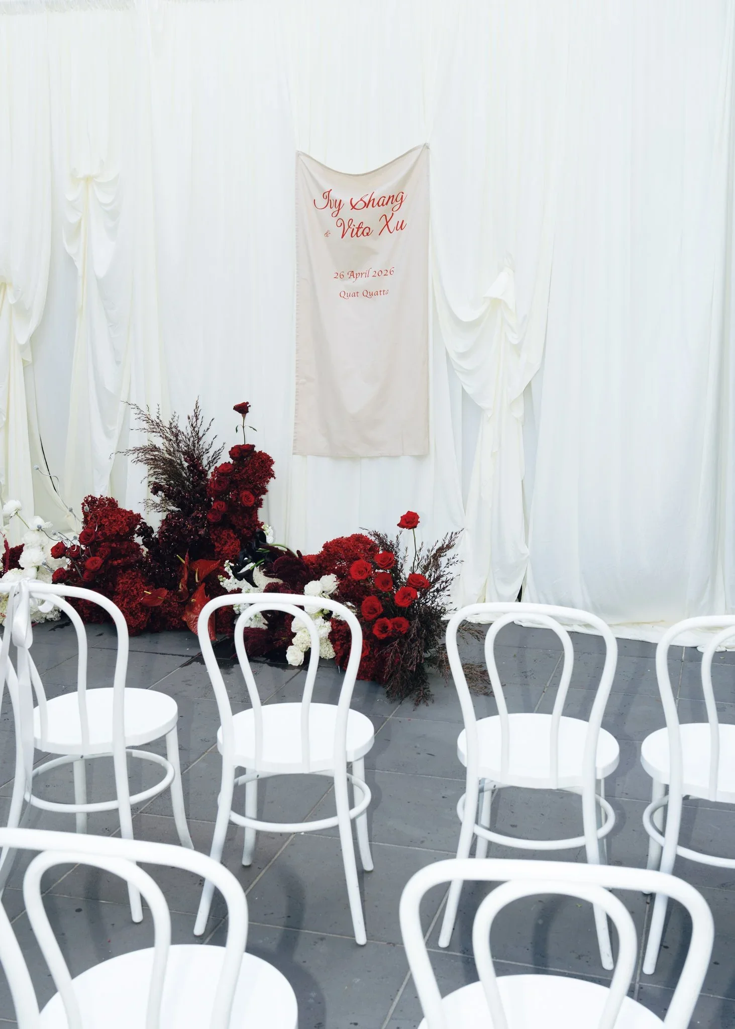Empty white chairs in front of a wedding backdrop with red and white flowers