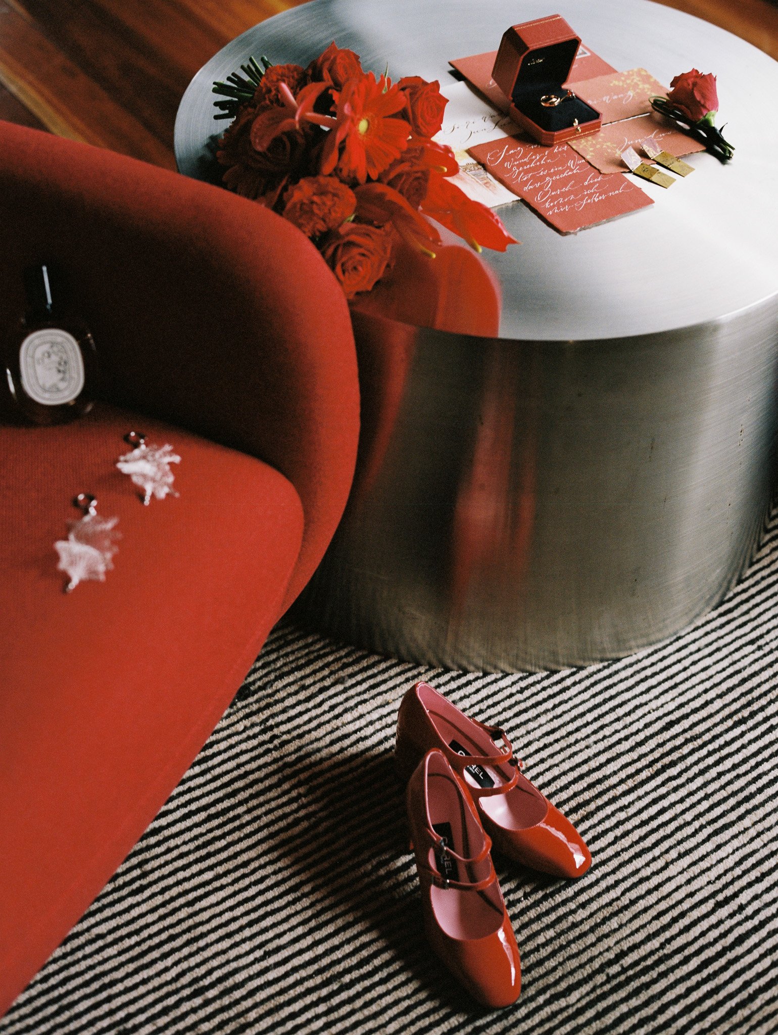 A coffee table with a bouquet of red flowers, a red jewelry box, handwritten love notes, a single red rose, and a pair of red high-heeled shoes.