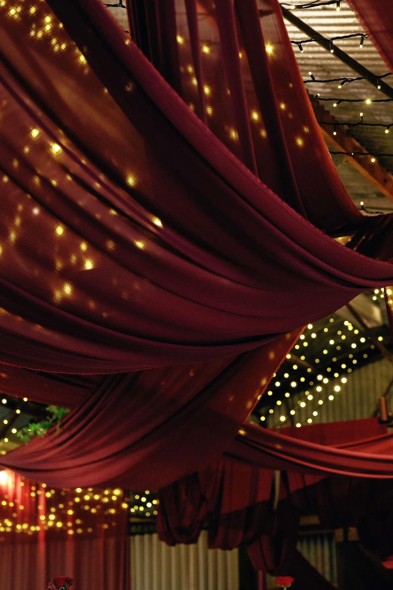 Close-up of a red umbrella with small yellow string lights underneath it, and more yellow string lights hanging in the background.