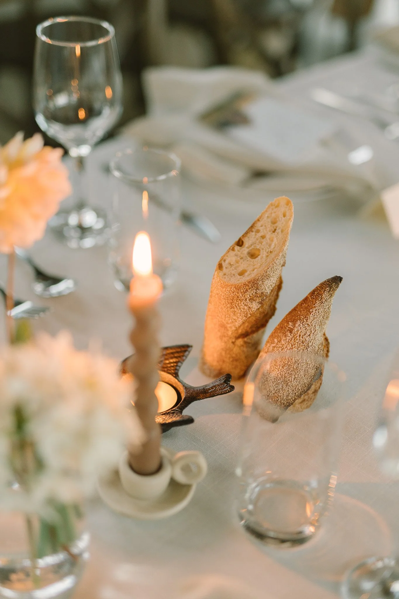 Close-up of breadsticks on a table with wine glasses, a candle, and a table setting in the background.