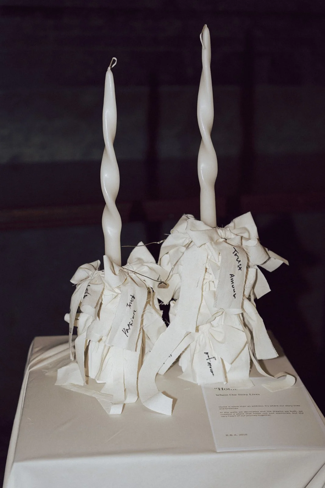 Art piece created with two twisted white candles atop a base of crumpled white paper with handwritten notes.