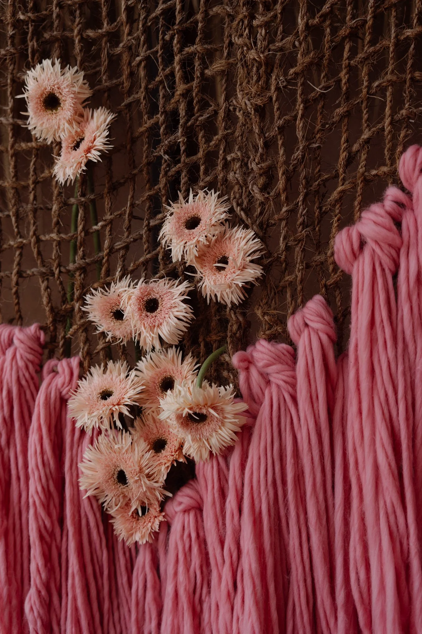 Pink flowers, a rope net, and pink yarn hanging against a wall.