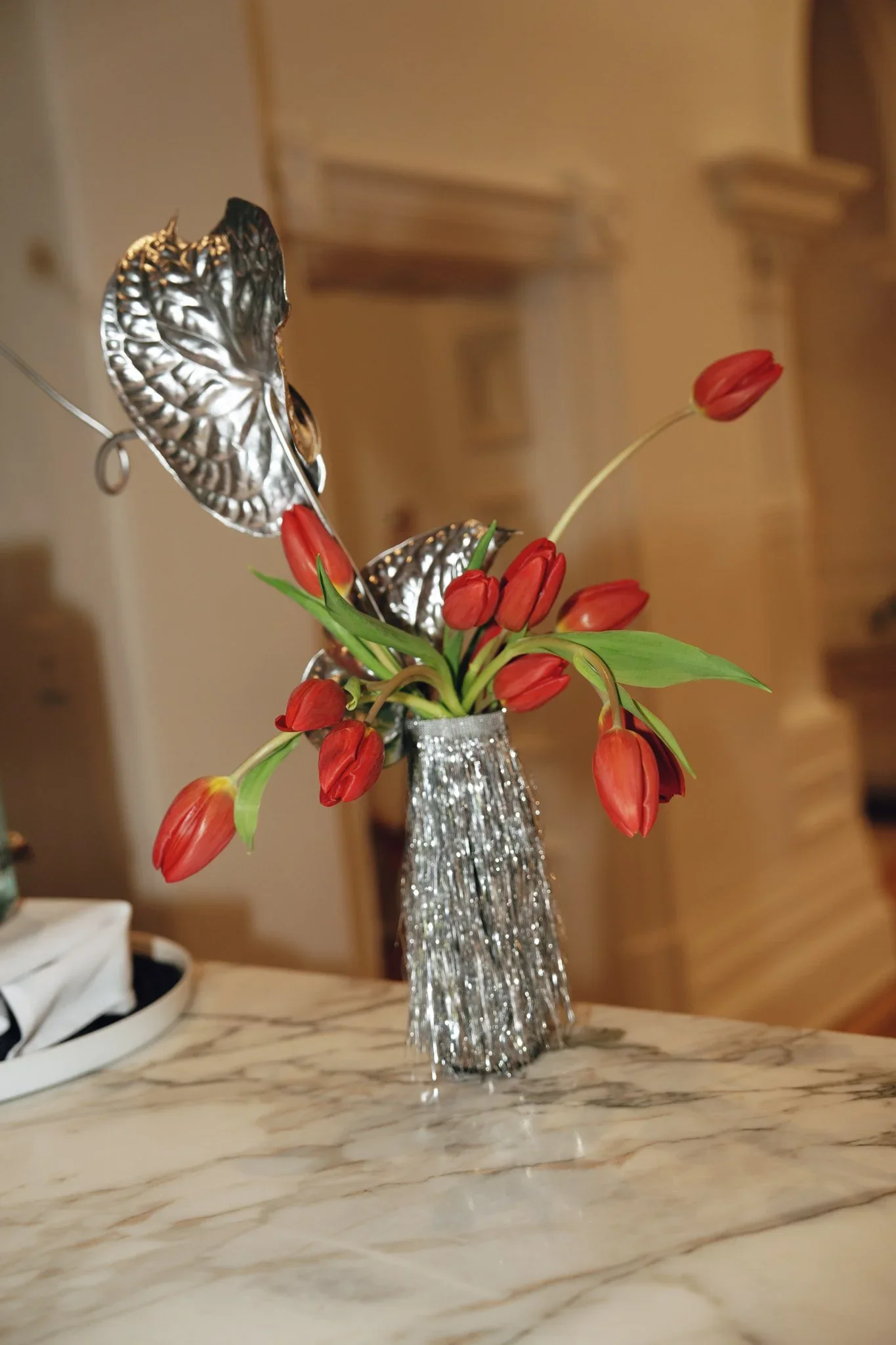 A silver vase holding a bouquet of red tulips on a marble table.