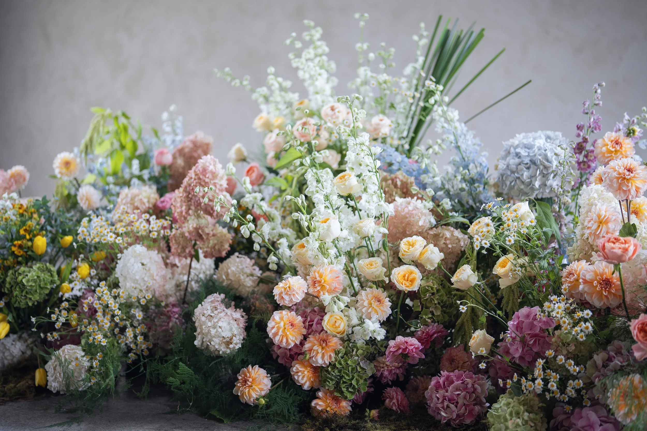 A large assortment of various colorful flowers arranged together, including roses, hydrangeas, daisies, and other floral blooms, in shades of pink, white, yellow, and orange.