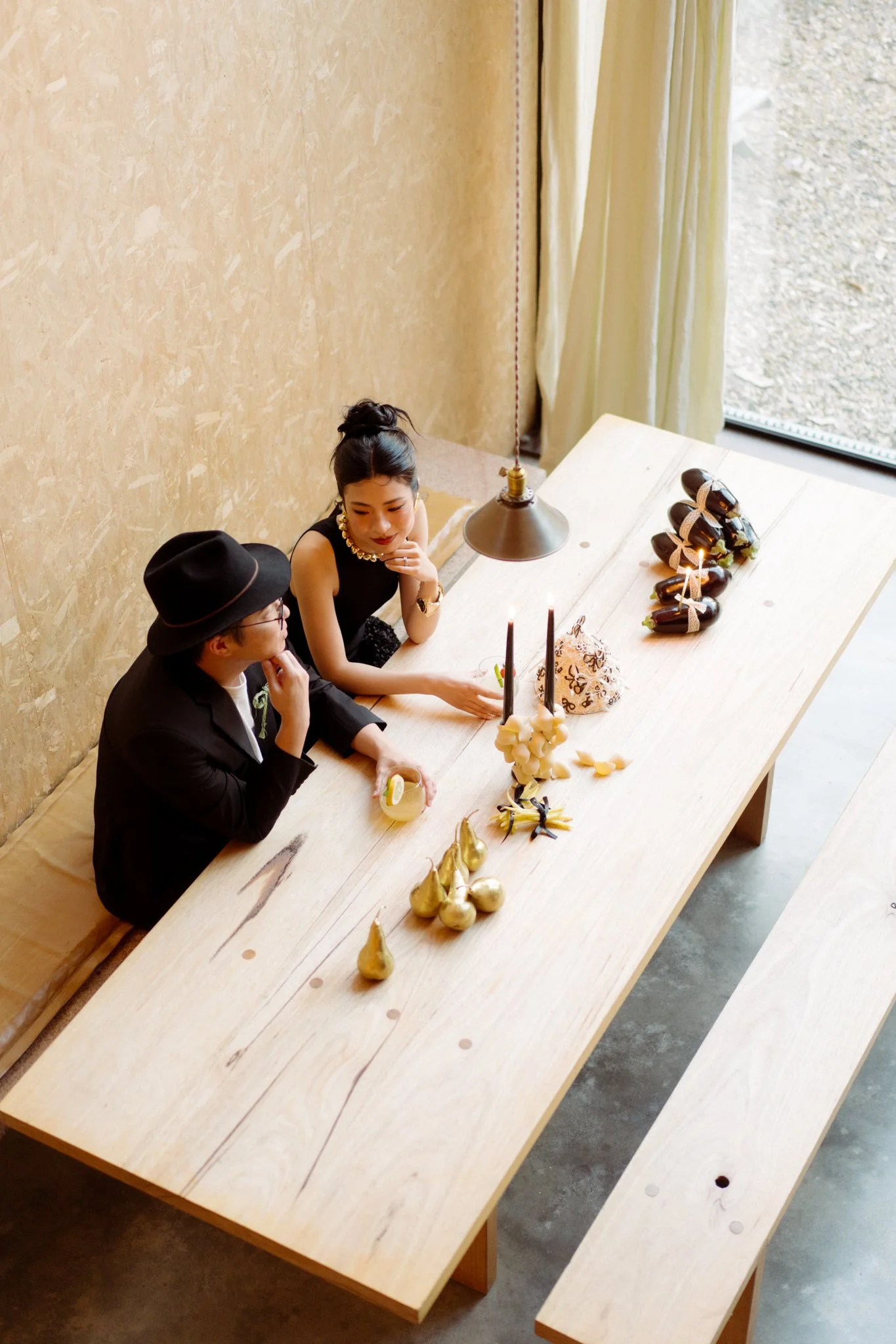 Two women sitting at a long wooden table decorated for a celebration with candles and gold ornaments, having a conversation.