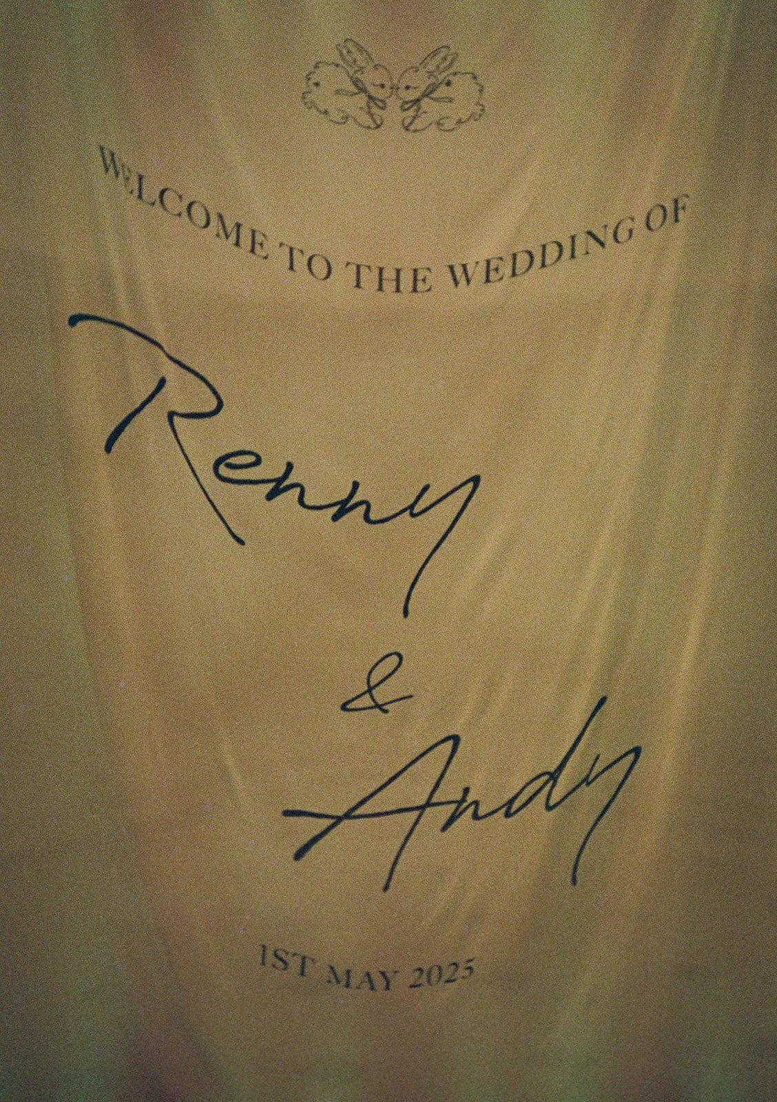 Wedding invitation card with the text 'Welcome to the wedding of Renny & Andry' and the date '1st May 2025'. There is an illustration of two bunnies at the top.