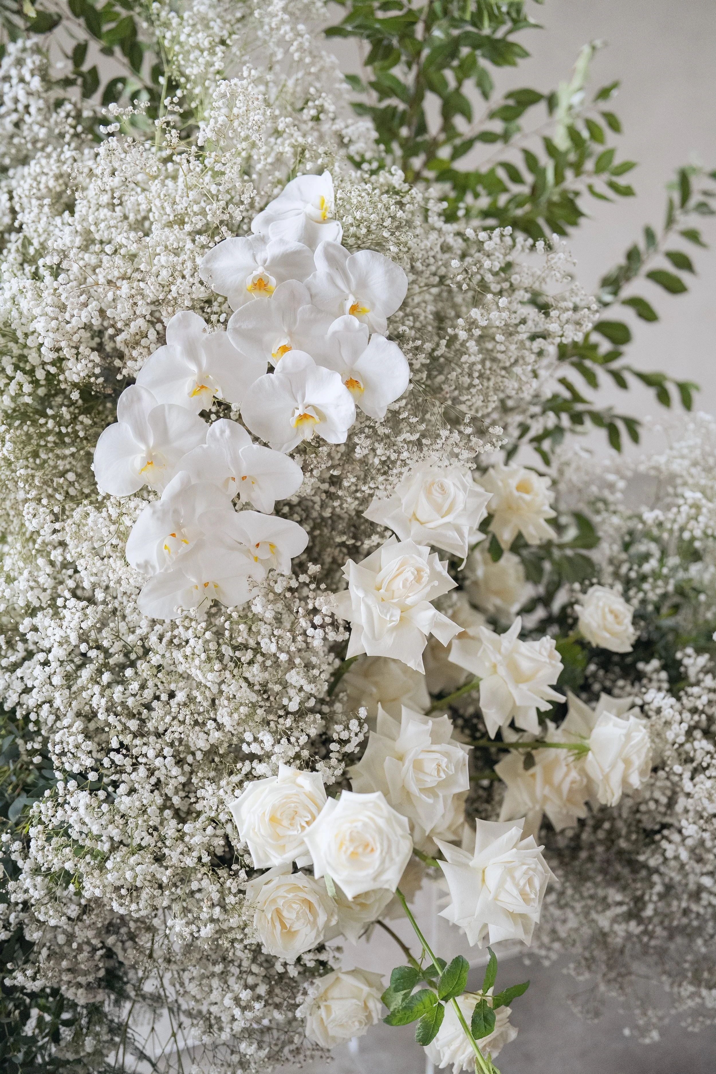 A bouquet of white orchids, roses, and baby's breath flowers with green leaves.
