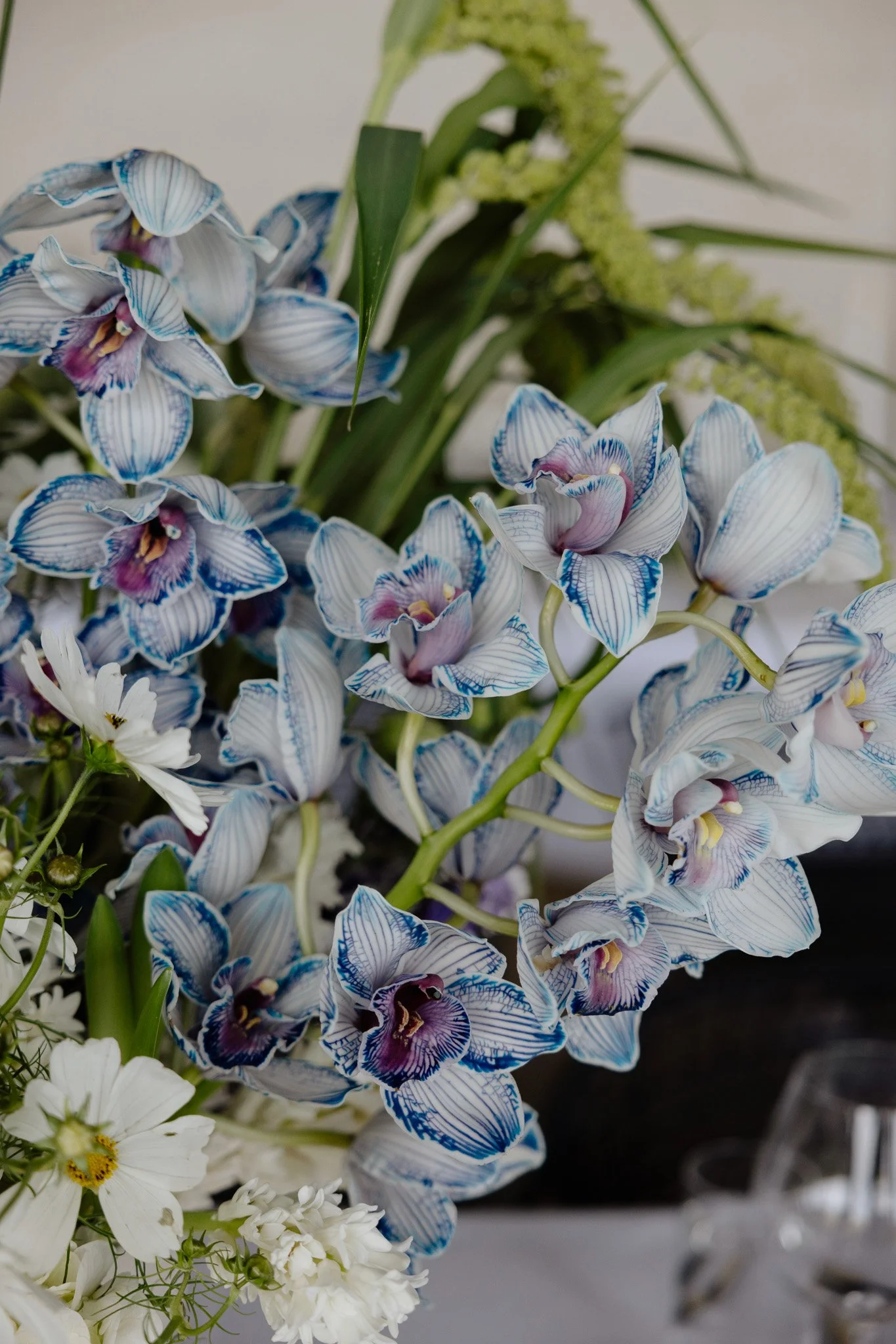 Close-up of a bouquet with blue and white orchids, accompanied by white and green flowers and foliage.