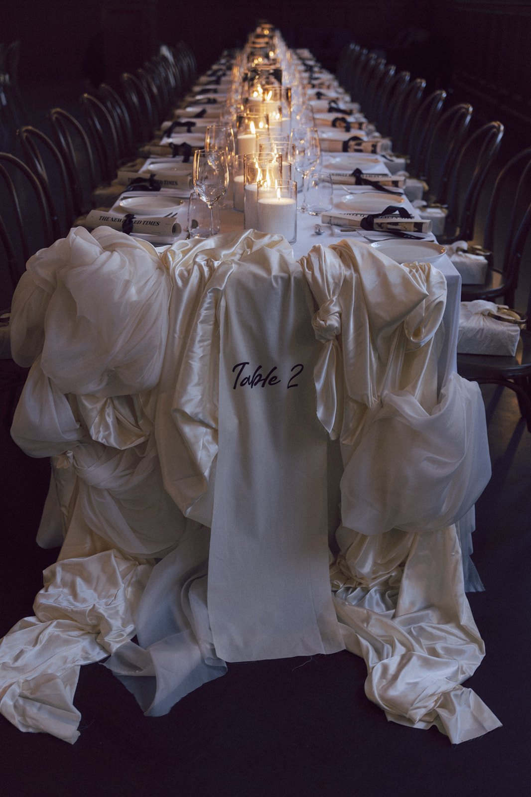 A long banquet table set for a formal event with candles, glasses, and napkins, marked as 'Table 2' with a white cloth covering the front of the table.