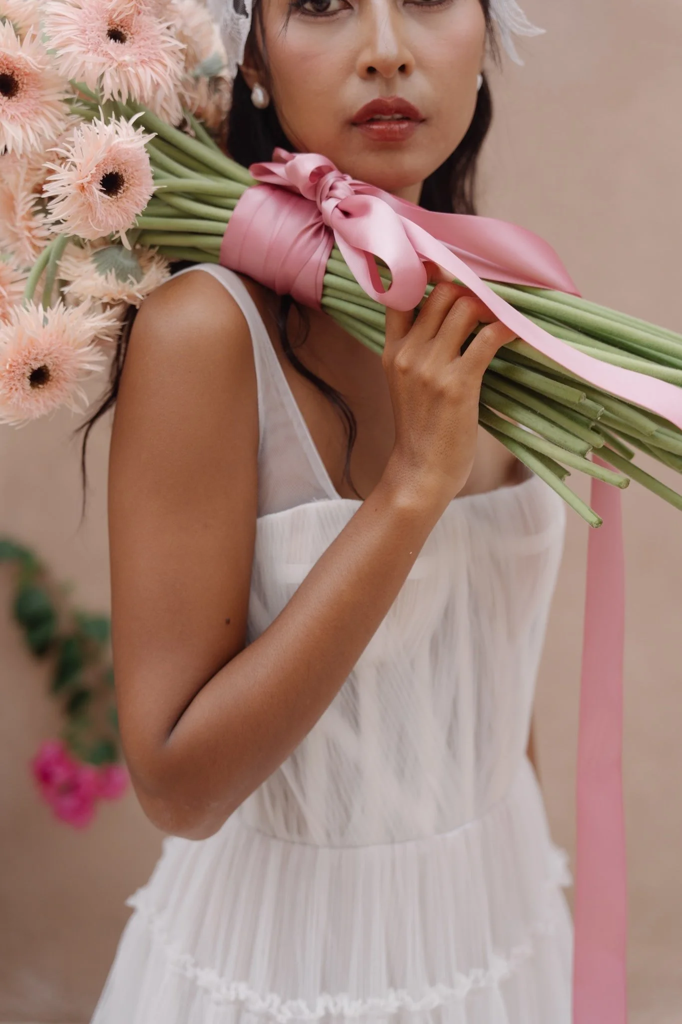 Woman holding a bouquet of pink flowers with a pink ribbon, wearing a white dress with ruffles.