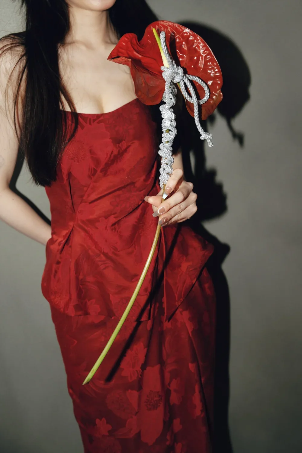 Woman in a red dress holding an artificial red anthurium flower with a silver rope tied around its stem.