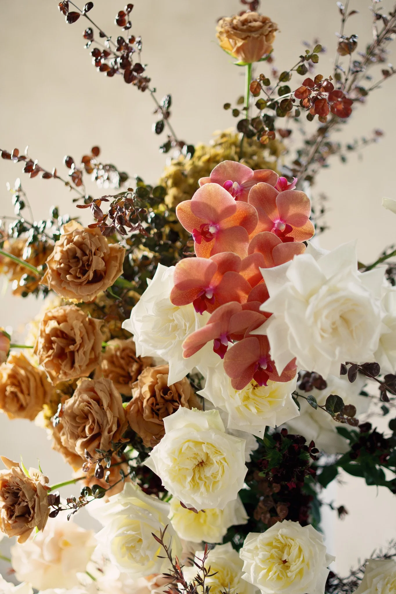 A floral arrangement with various flowers, including white roses, pink orchids, and brownish dried flowers, with dark purple branches in the background.