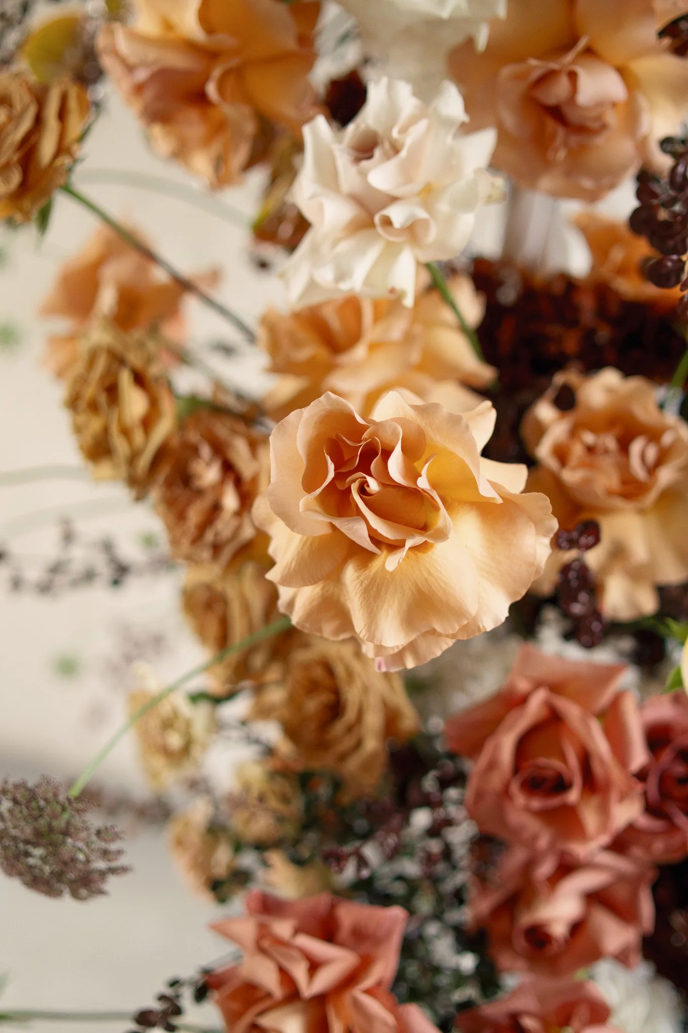 Close-up of various dried flowers in shades of white, peach, and pink, with some dark purple and green stems visible, arranged in a bouquet.