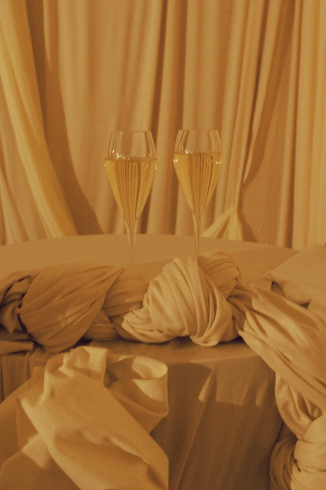 Two glasses of champagne on a table with a decorative cloth, golden curtains in the background.