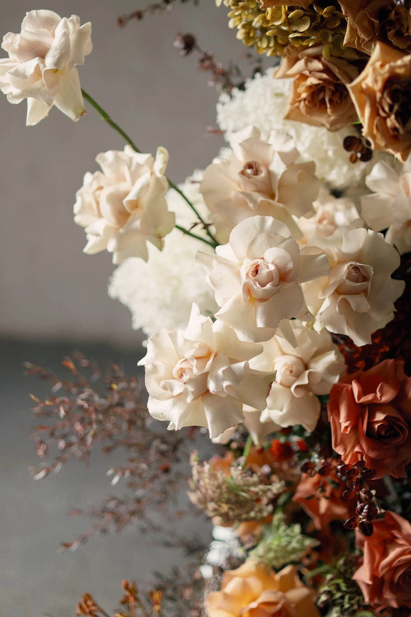 A colorful arrangement of flowers including white roses and beige and rust-colored flowers, with some small dark berries and blurred foliage in the background.