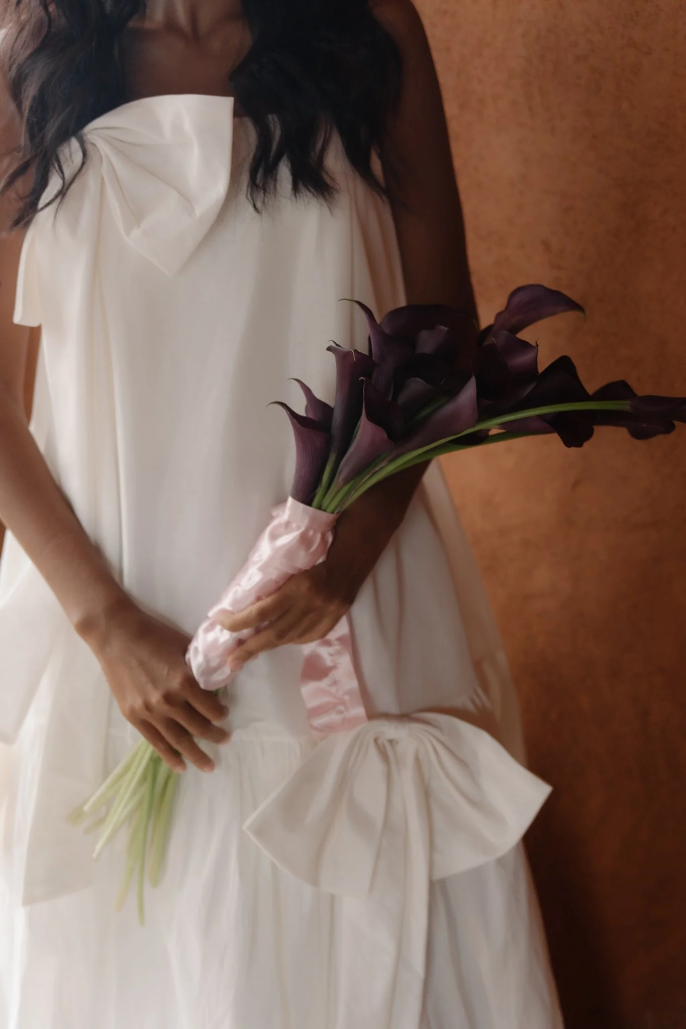 Woman in white dress holding a bouquet of dark purple calla lilies.