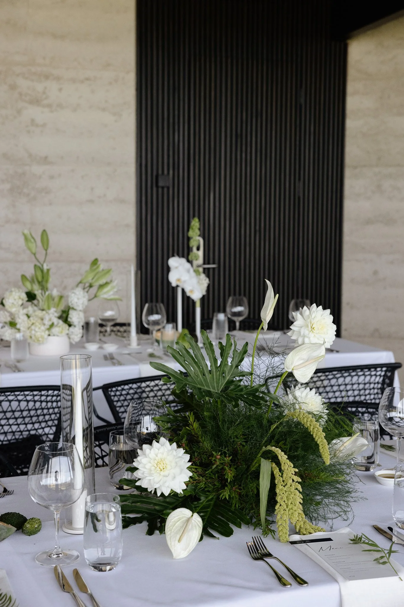 A table decorated with a flower centerpiece, surrounded by wine glasses, silverware, and a white tablecloth, set for a formal event.