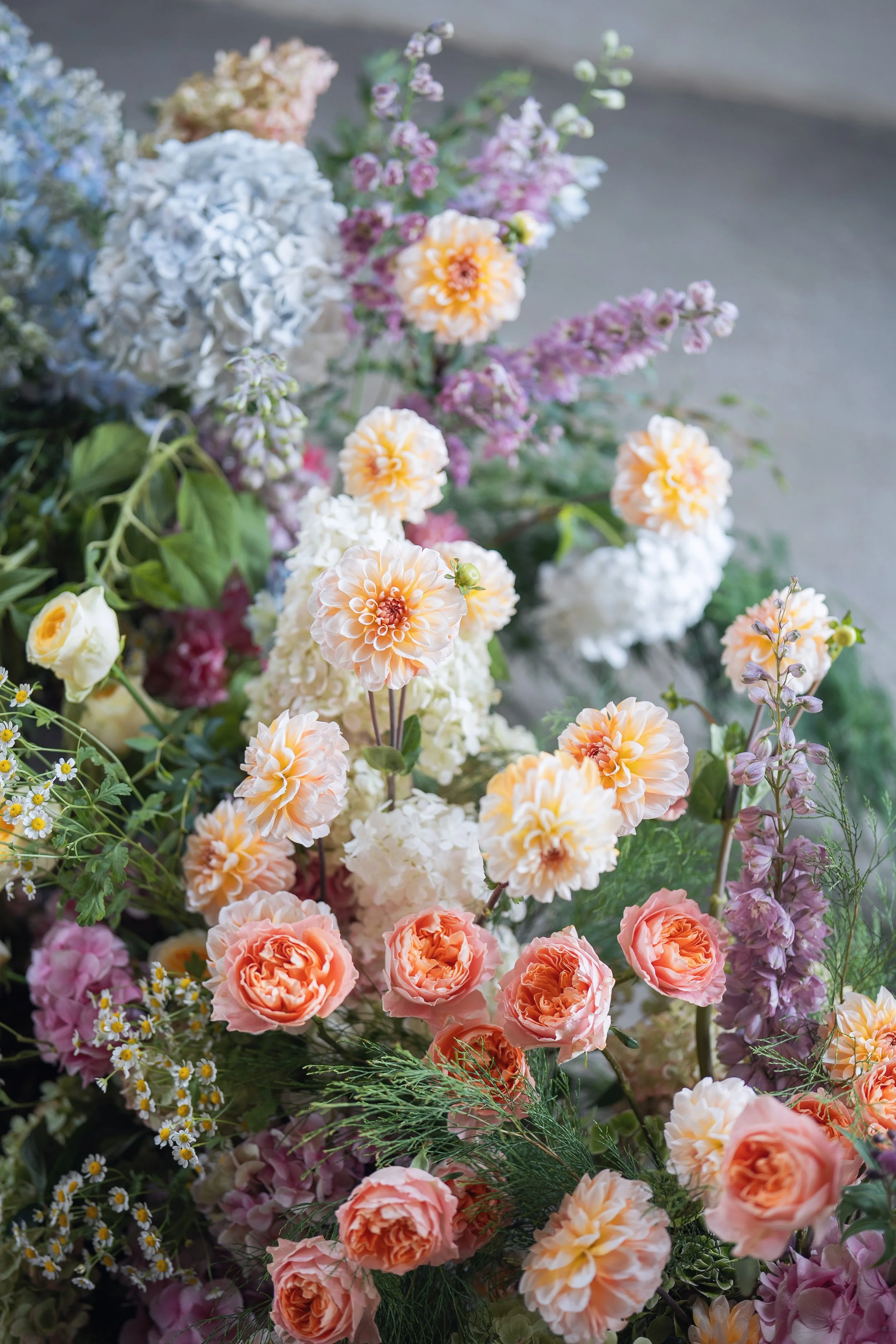 An assortment of colorful flowers including dahlias, roses, and wildflowers in shades of orange, pink, white, purple, and yellow.