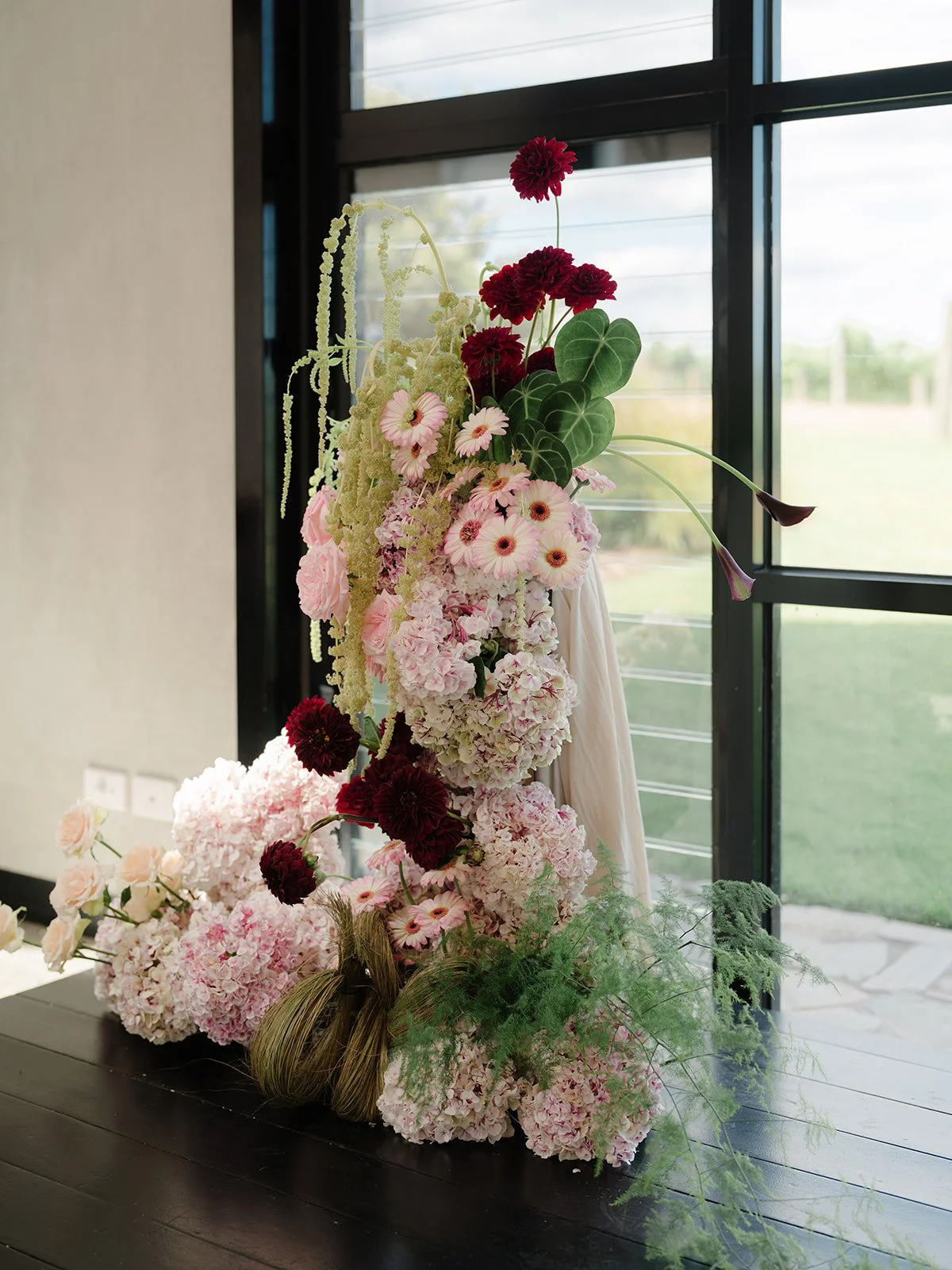 Arranged floral display of pink and red flowers near a window with greenery outside.