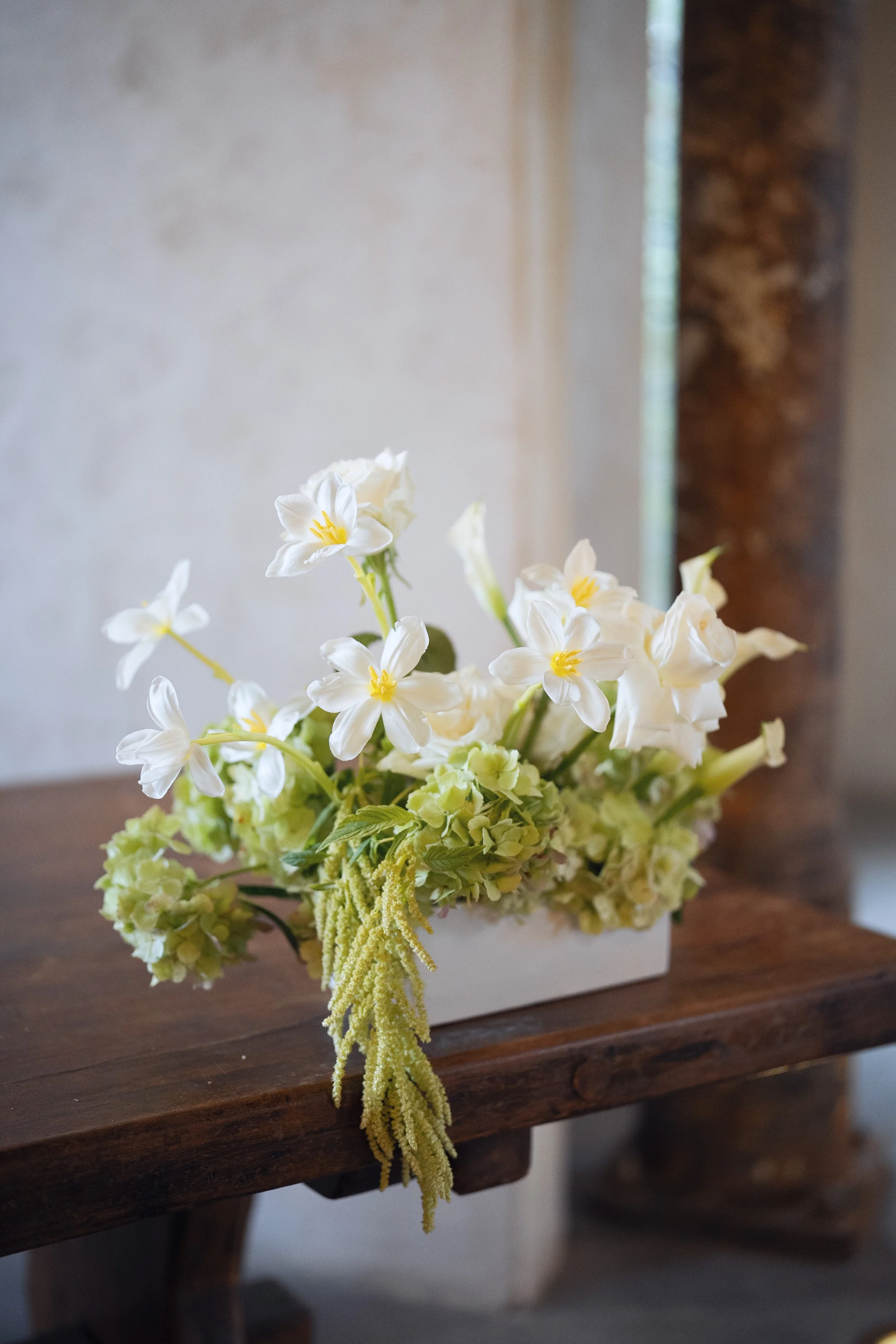 A bouquet of white and yellow flowers sitting on a wooden table with a blurred background.